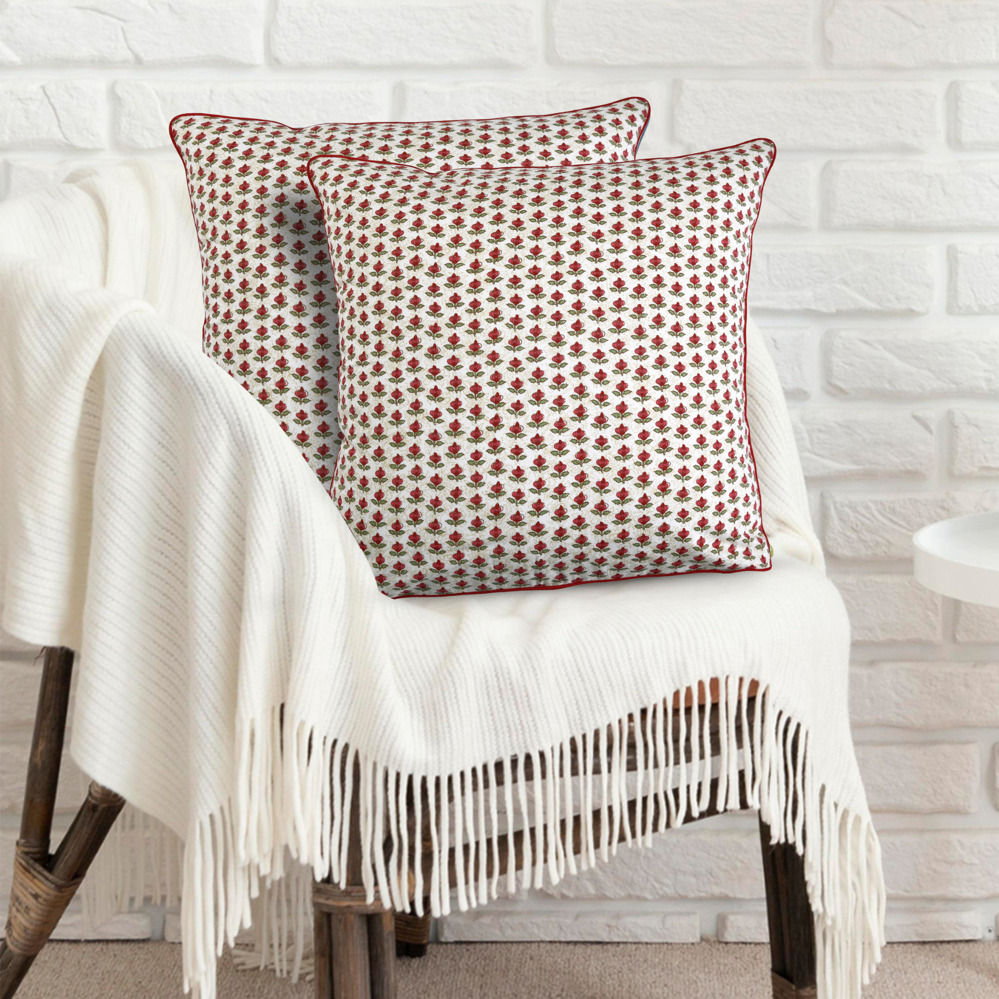 Decorative pillow with red pattern on a white chair against a white brick wall.