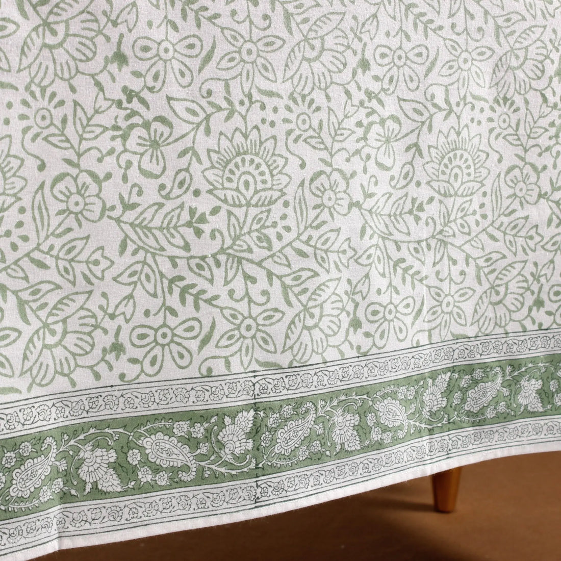 Floral patterned tablecloth with green and white colors on a wooden surface.