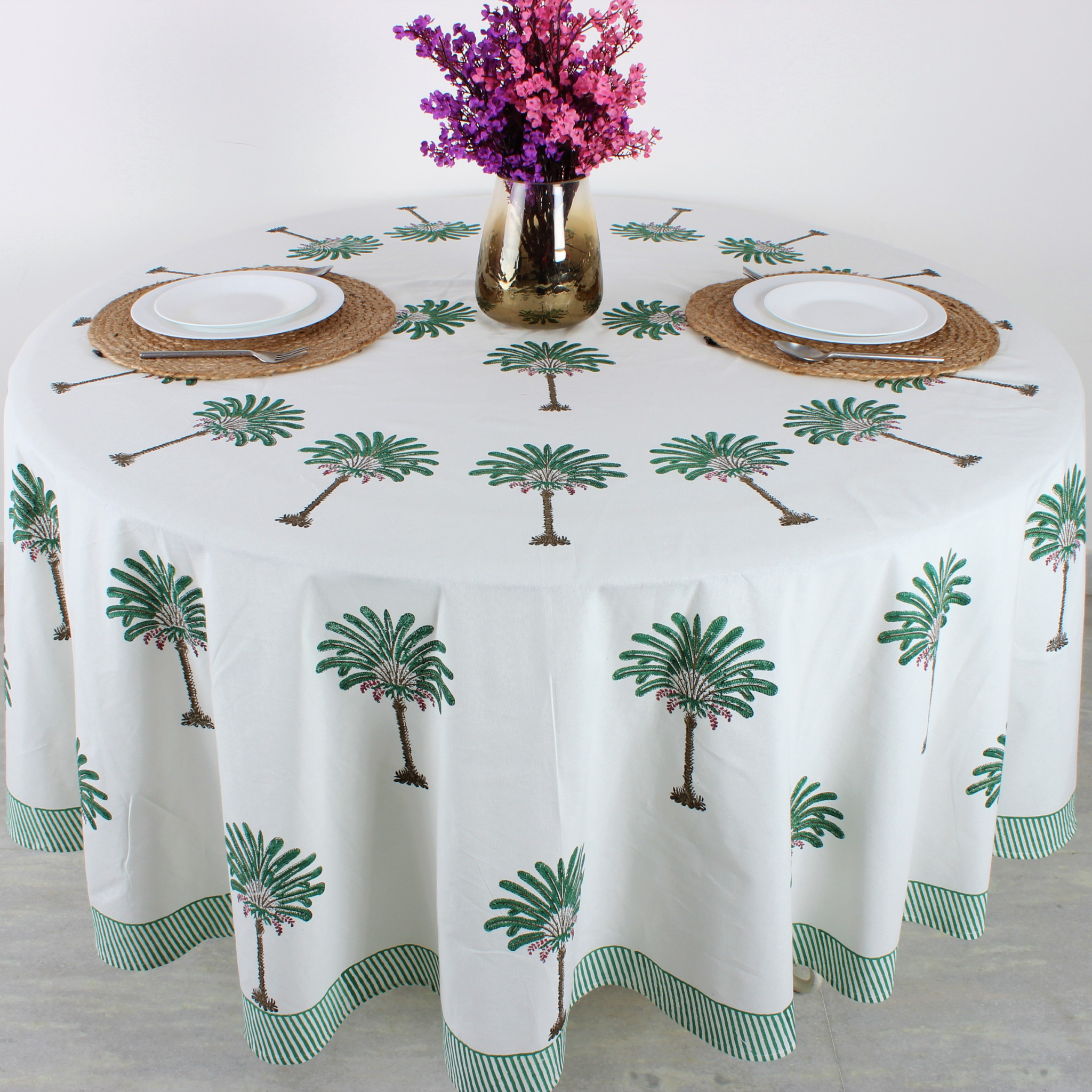 Tablecloth with palm tree design on a round table with place settings and flowers.
