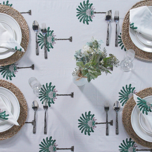 Table setting with white plates, silverware, and decorative tablecloth with palm tree pattern.
