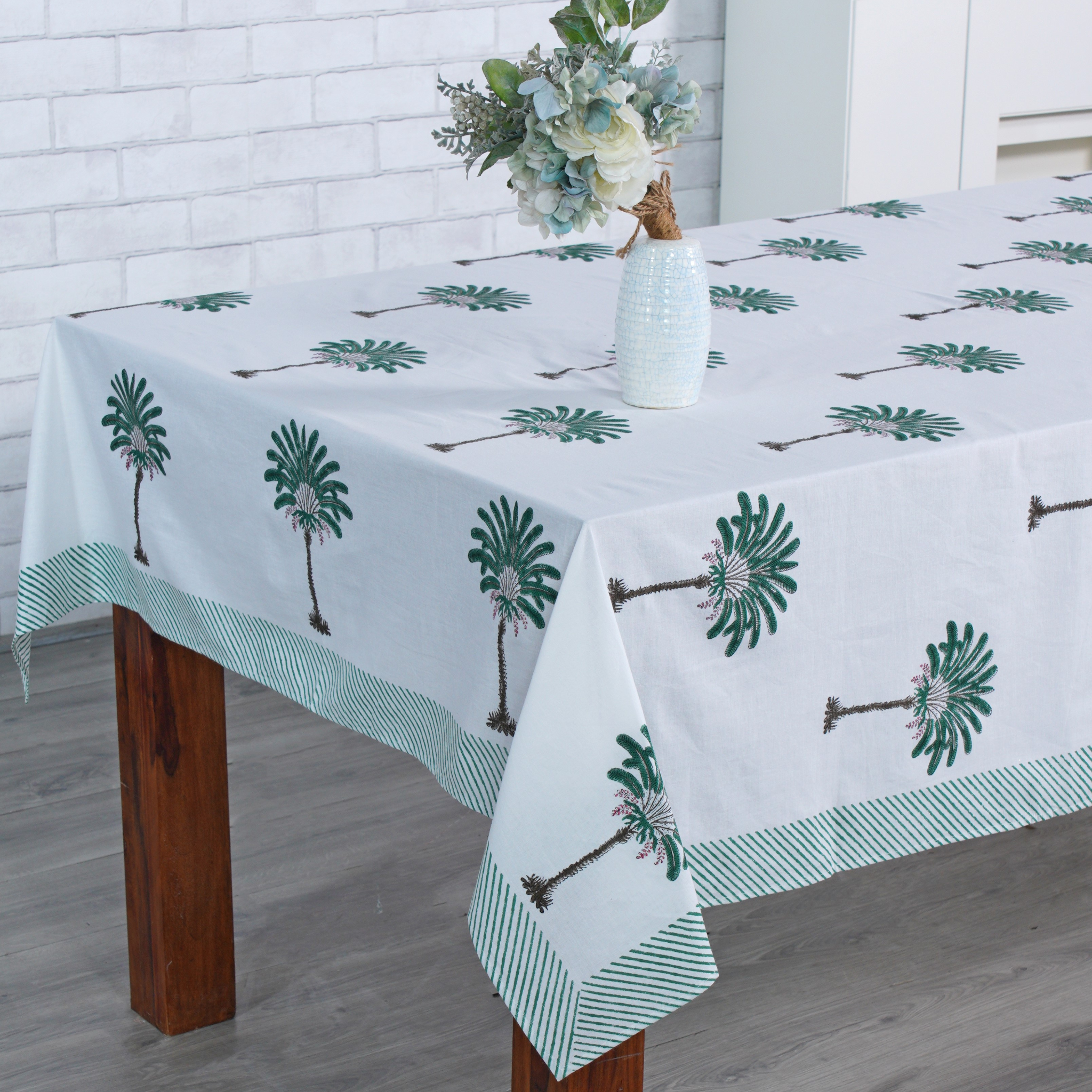 Tablecloth with palm tree design on a wooden table against a white brick wall.