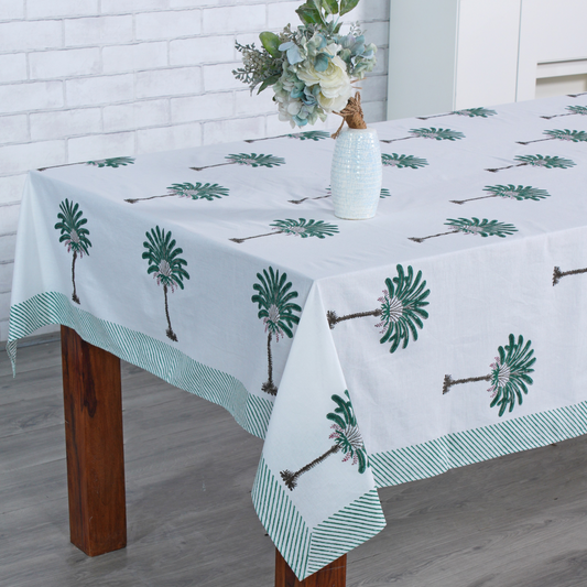 Tablecloth with palm tree design on a wooden table against a white brick wall.