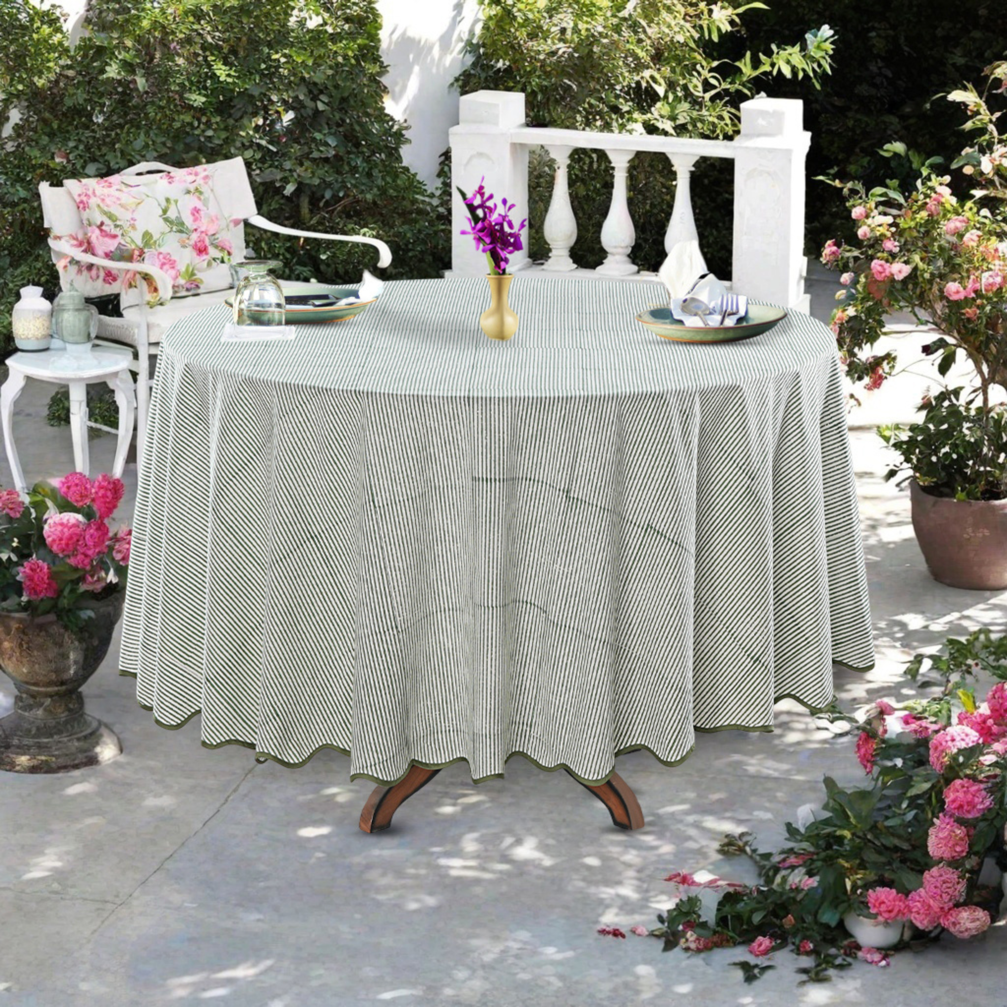 Round table with a striped tablecloth in an outdoor setting with flowers and chairs.