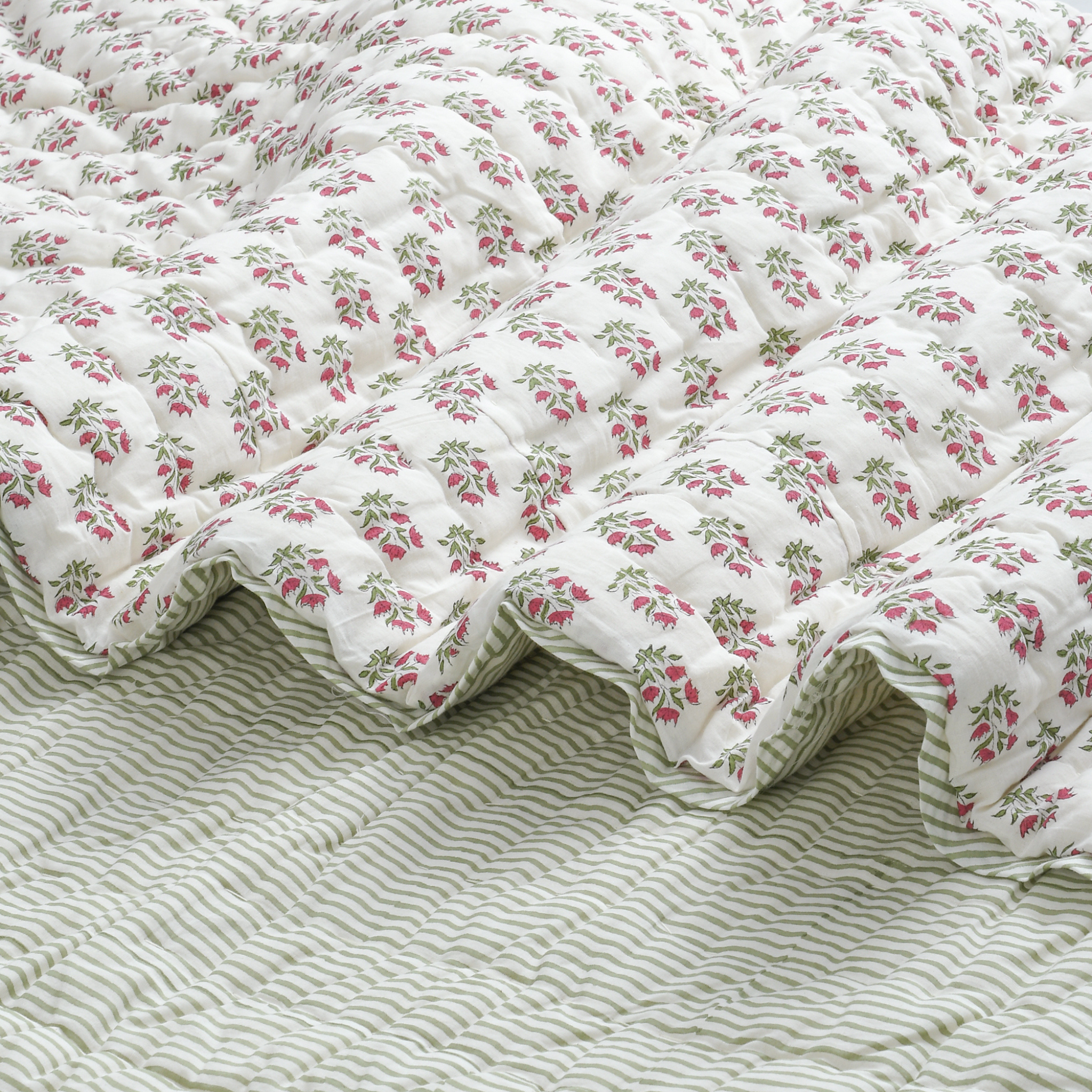 Floral quilt on a bed with a striped bedspread