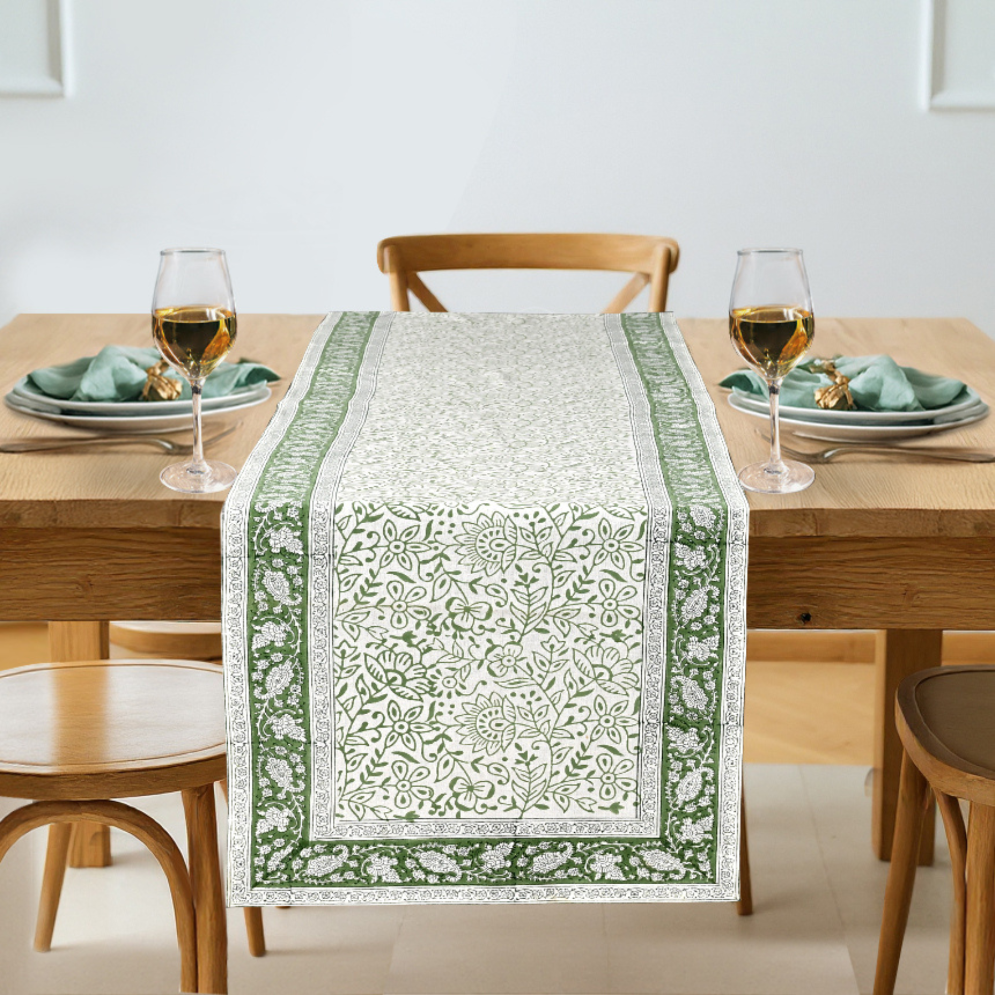 Dining table set with a green and white patterned table runner, glasses, and plates.