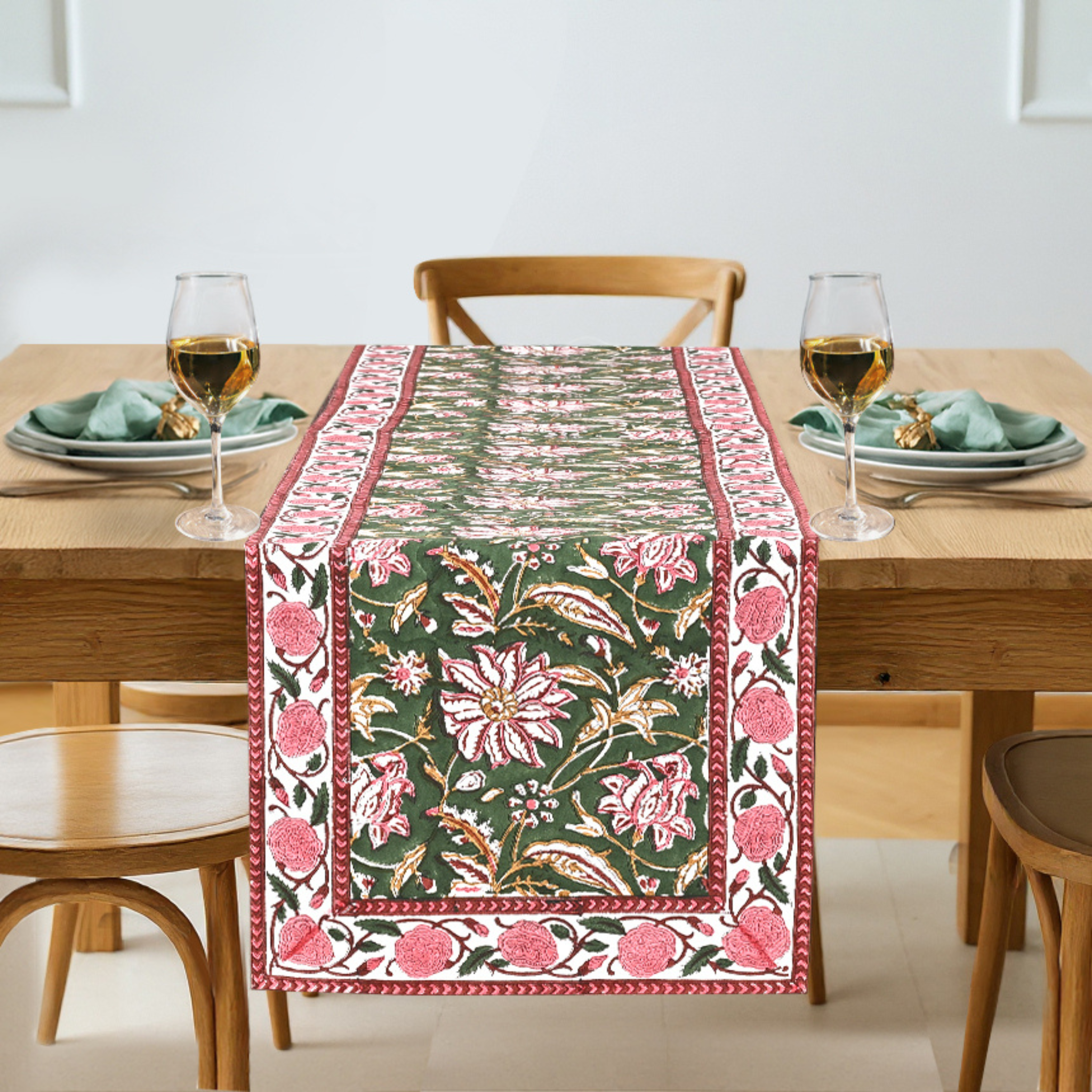 Decorative floral table runner on a wooden table with glasses and plates.