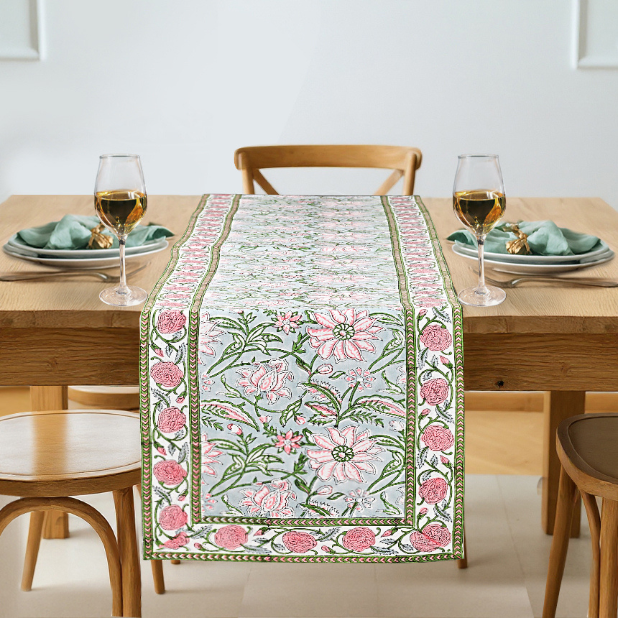 Floral table runner on a wooden table with glasses and plates.