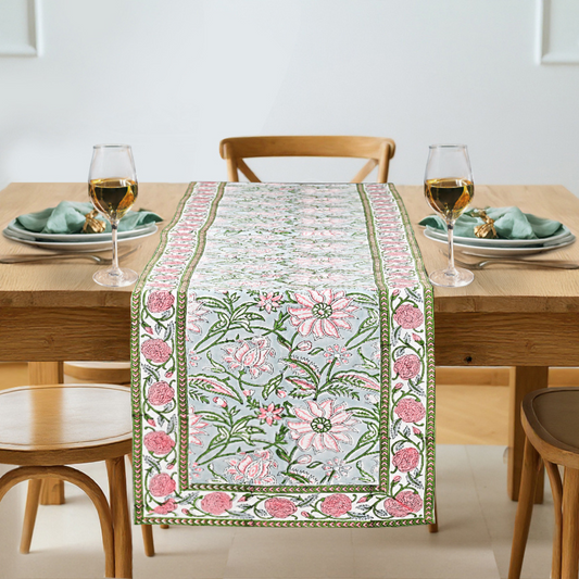 Floral table runner on a wooden table with glasses and plates.