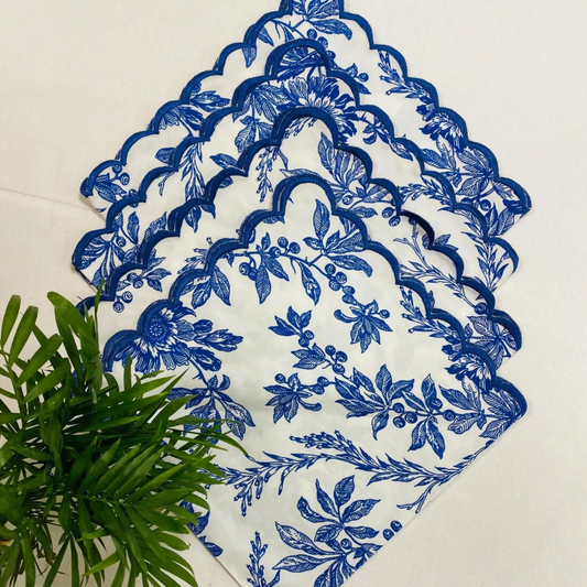 Blue floral patterned doily on a white surface with green leaves.