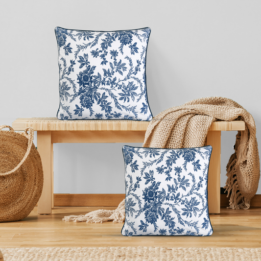 Two blue floral-patterned pillows on a wooden stool with a beige blanket and woven basket.