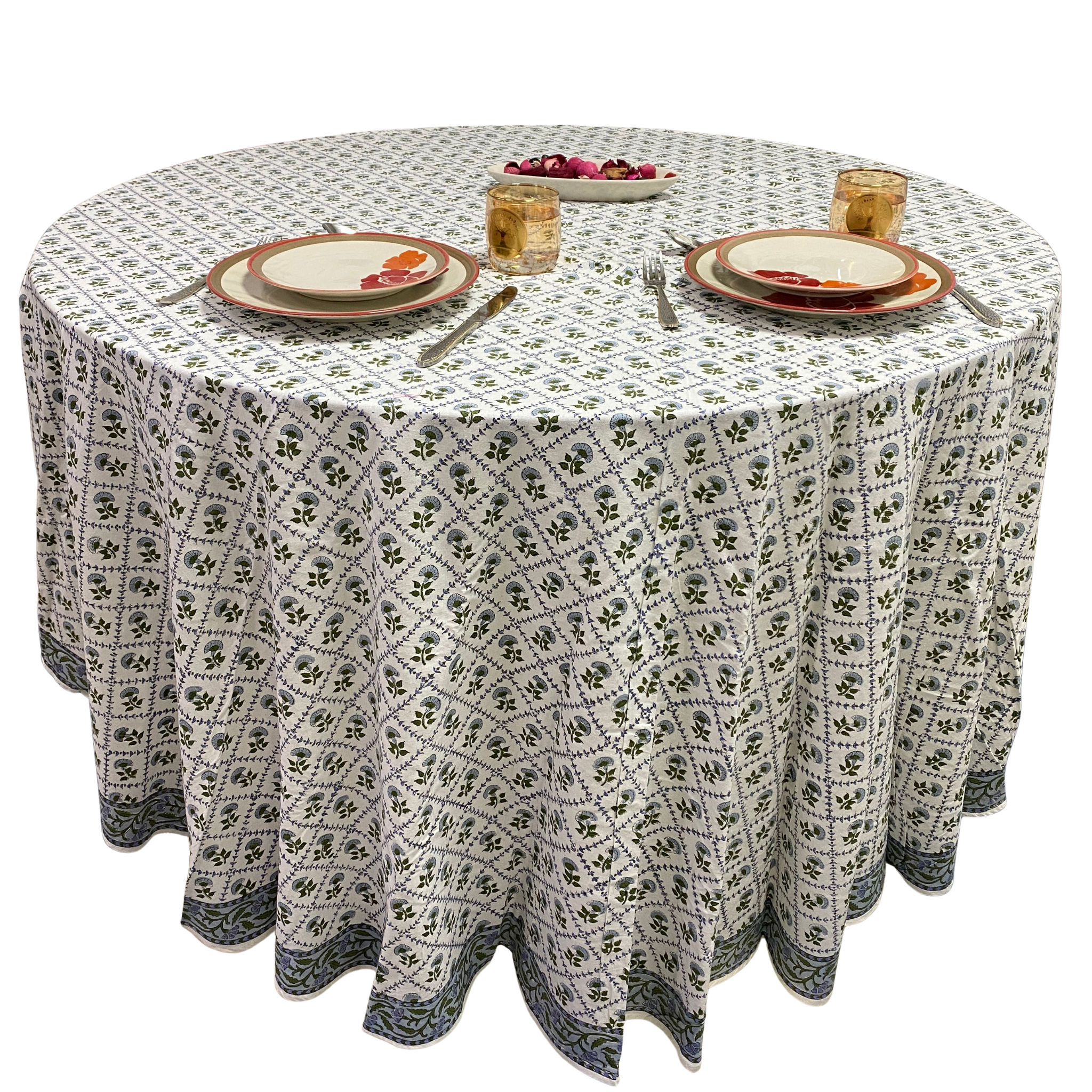 Round table with a patterned tablecloth, plates, and cutlery on a white background