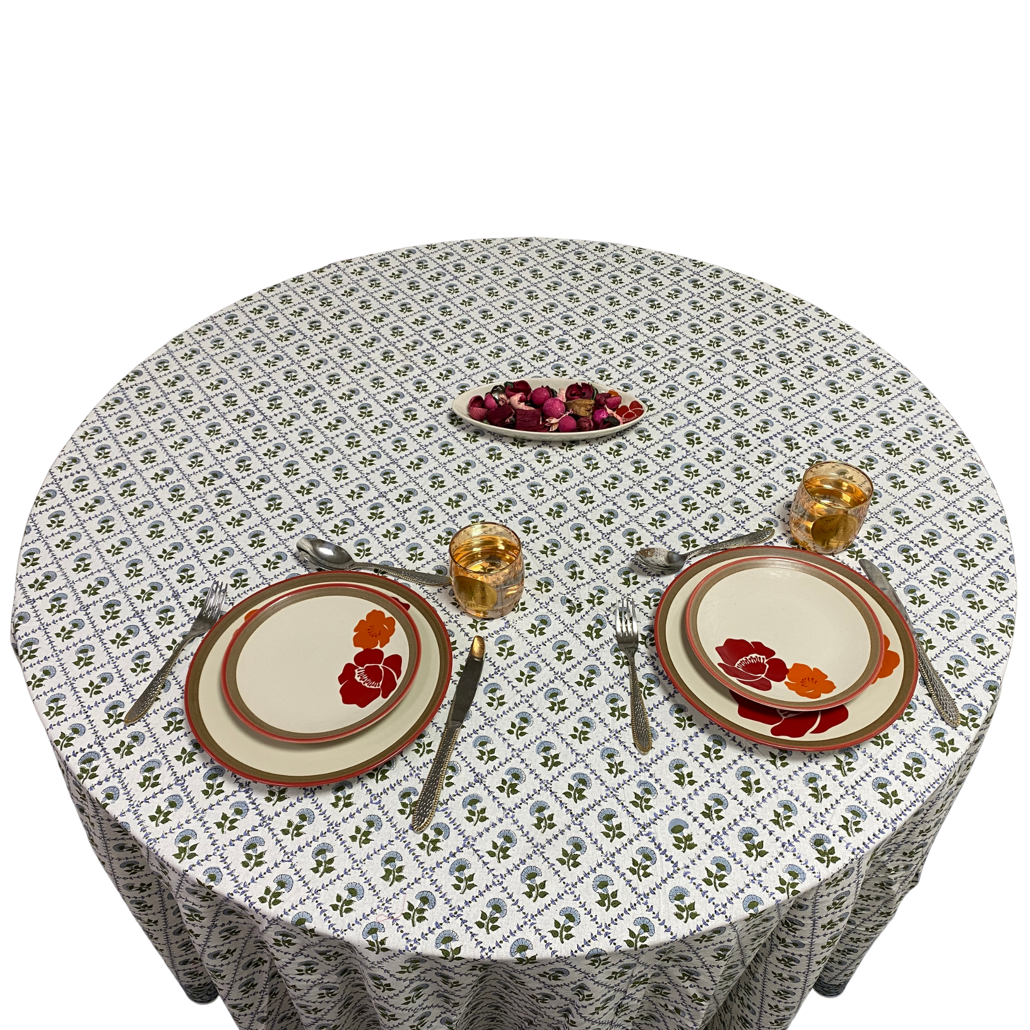 Round table set with floral tablecloth, plates, cutlery, and glasses on a white background