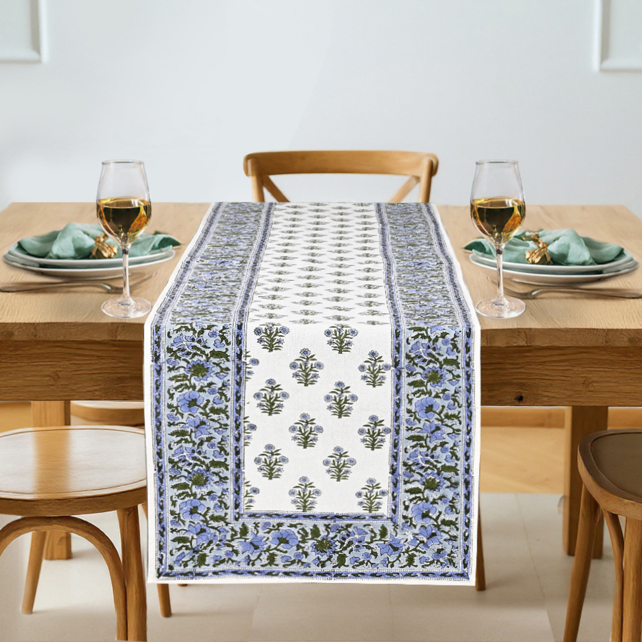 Dining table with a floral patterned table runner, glasses, and plates.