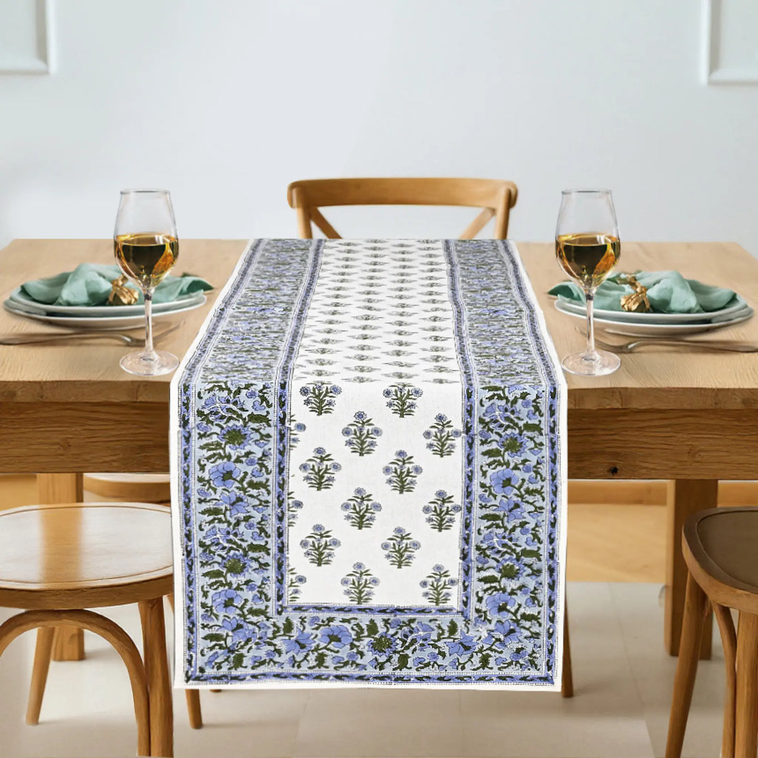 Dining table with a floral patterned table runner, glasses, and plates.