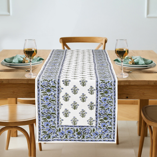 Dining table with a floral patterned table runner, glasses, and plates.