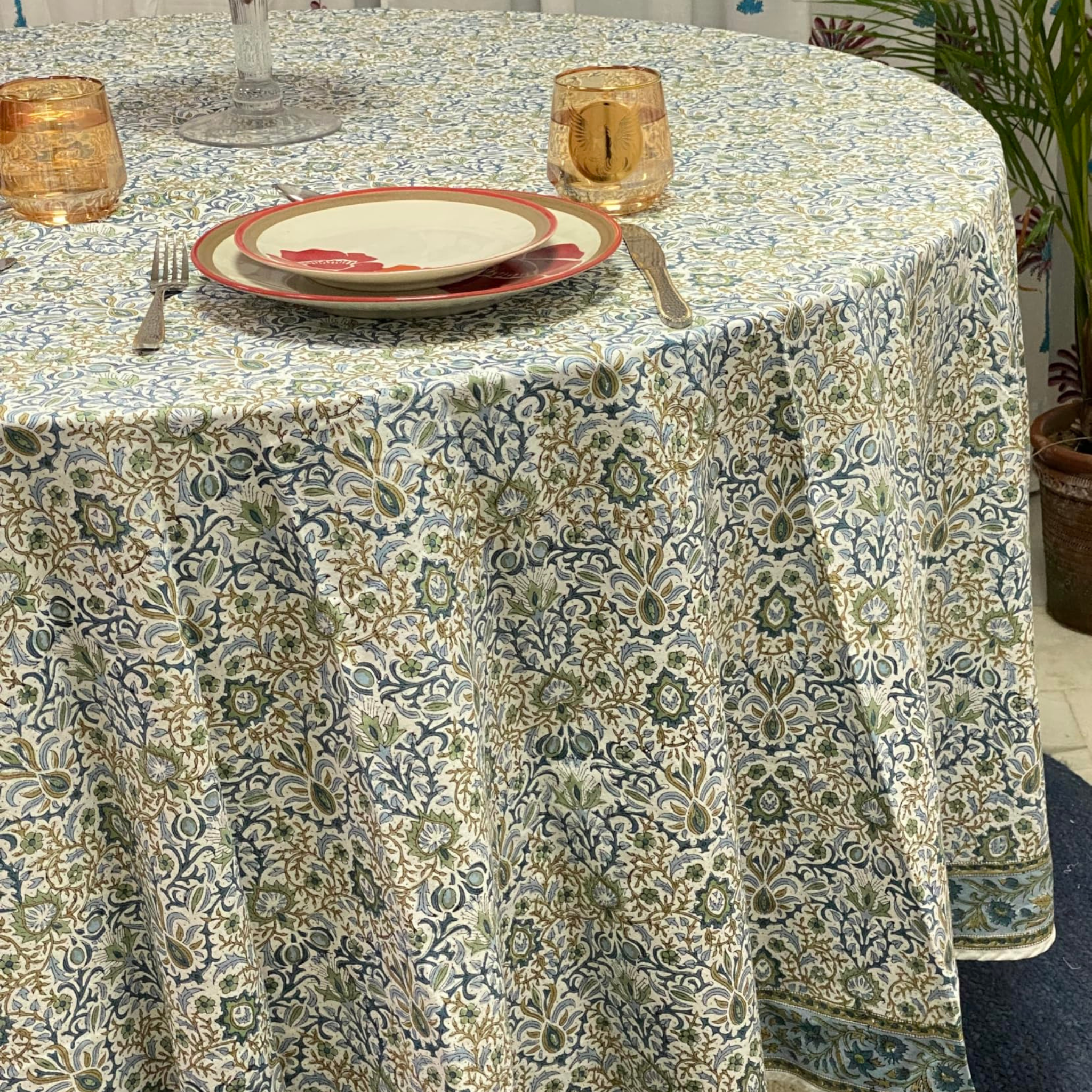 Patterned tablecloth on a round table with plates and glasses.