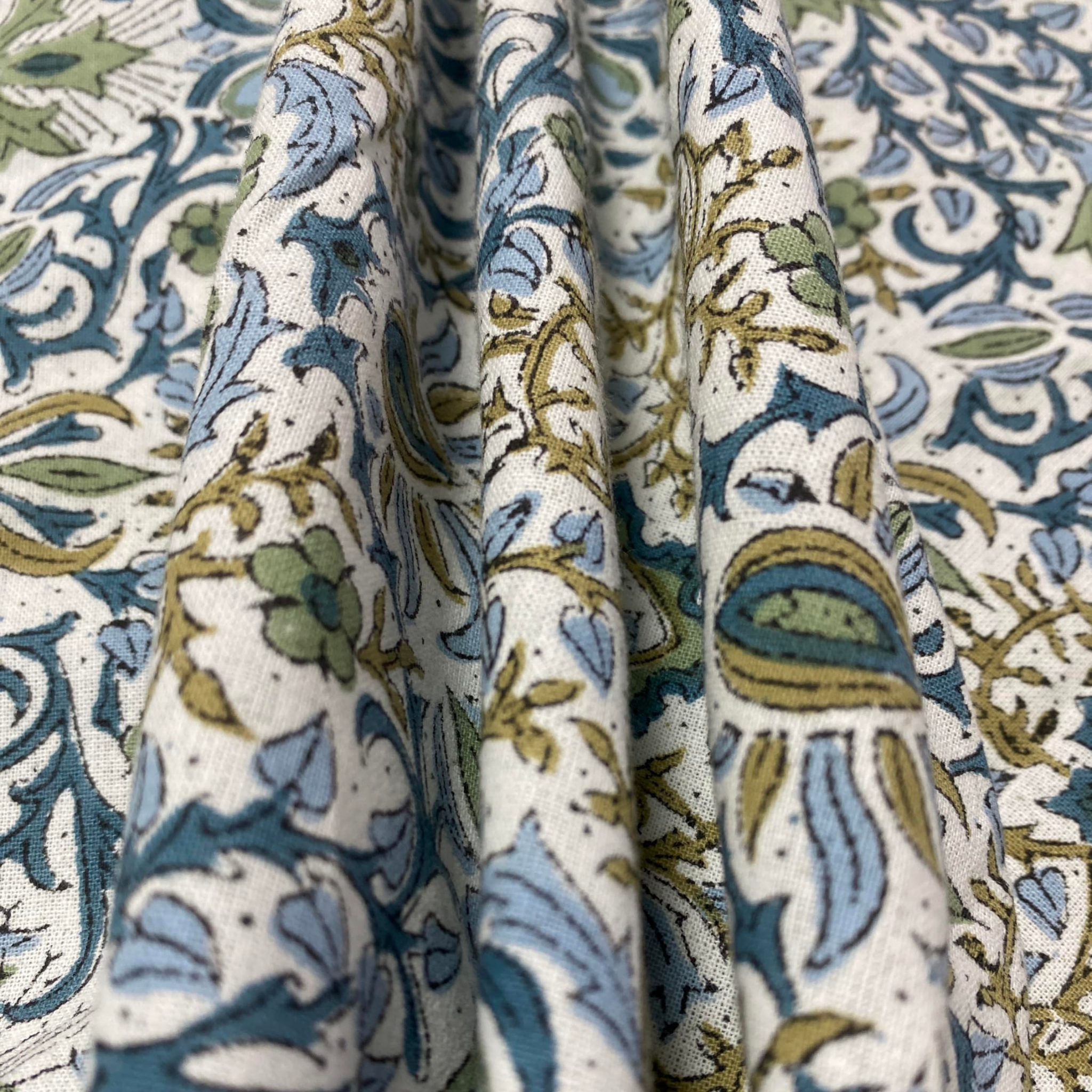 Close-up of patterned fabric with blue, green, and beige colors on a white background.
