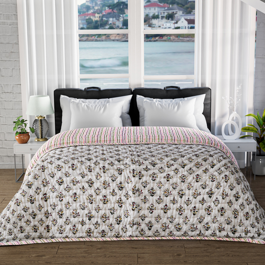 Bed with floral quilt and white pillows in a room with large windows showing a waterfront view.