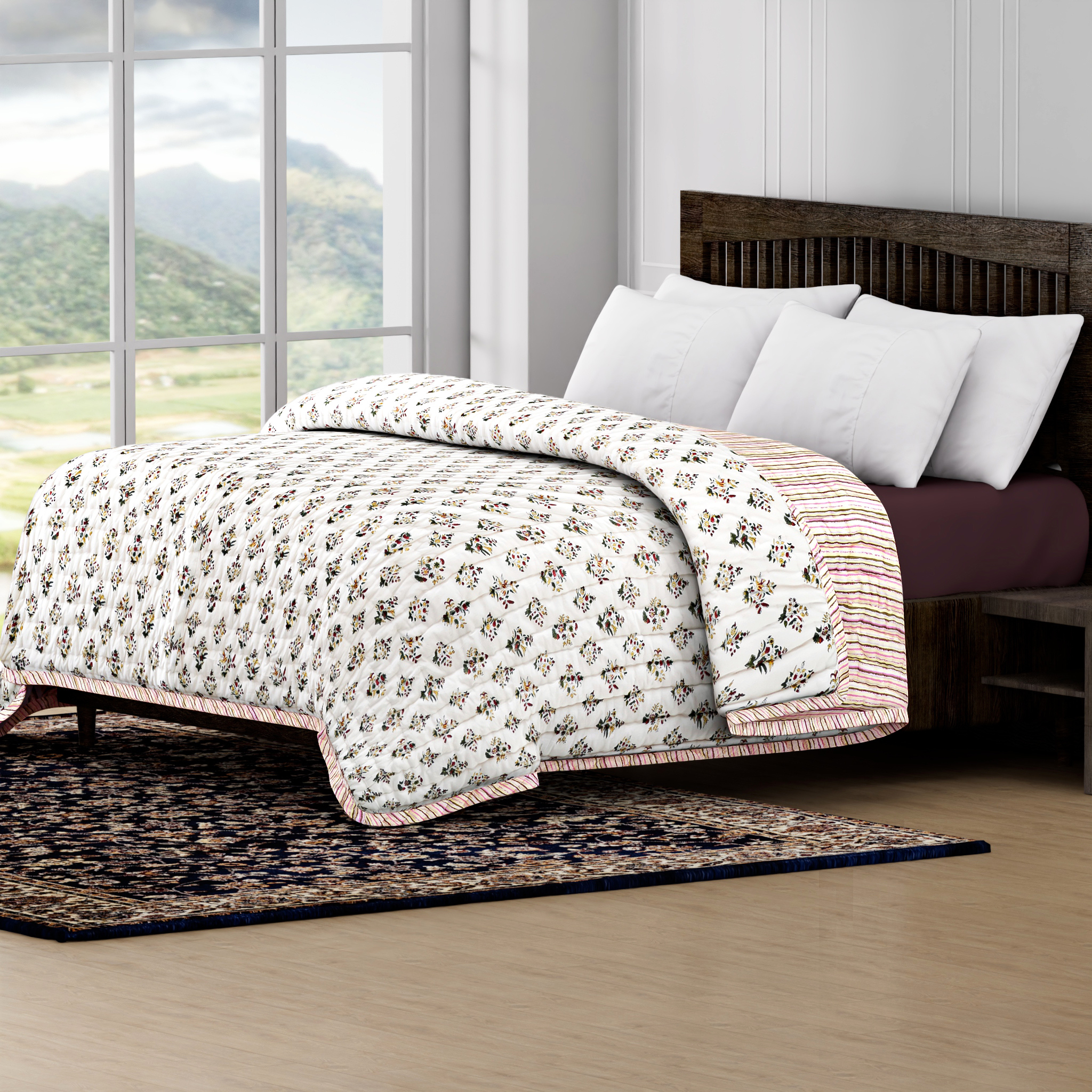 Bed with floral quilt and white pillows in a room with large windows showing a scenic view.