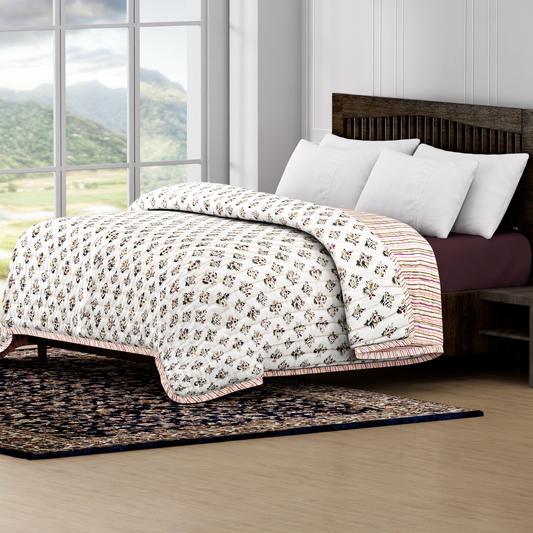 Bed with floral quilt and white pillows in a room with large windows showing a scenic view.