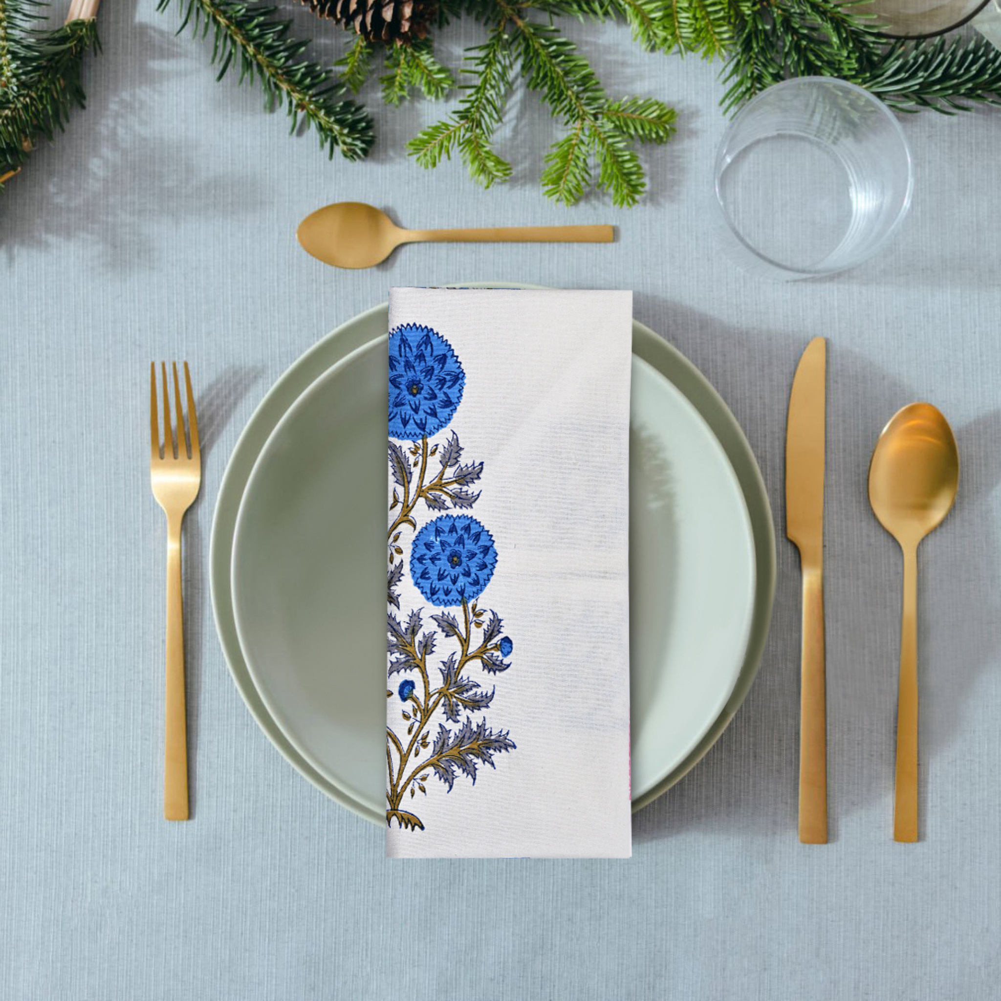 Table setting with a floral napkin, plates, cutlery, and Christmas decorations.