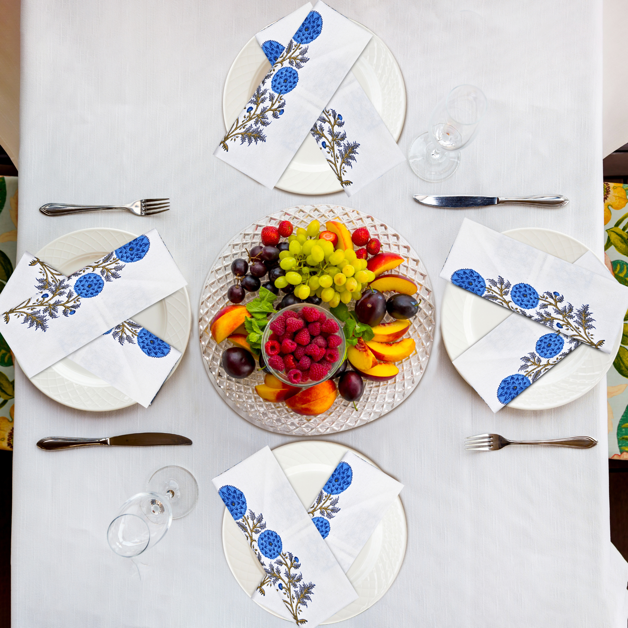 Table setting with fruit platter and floral napkins on a white tablecloth.