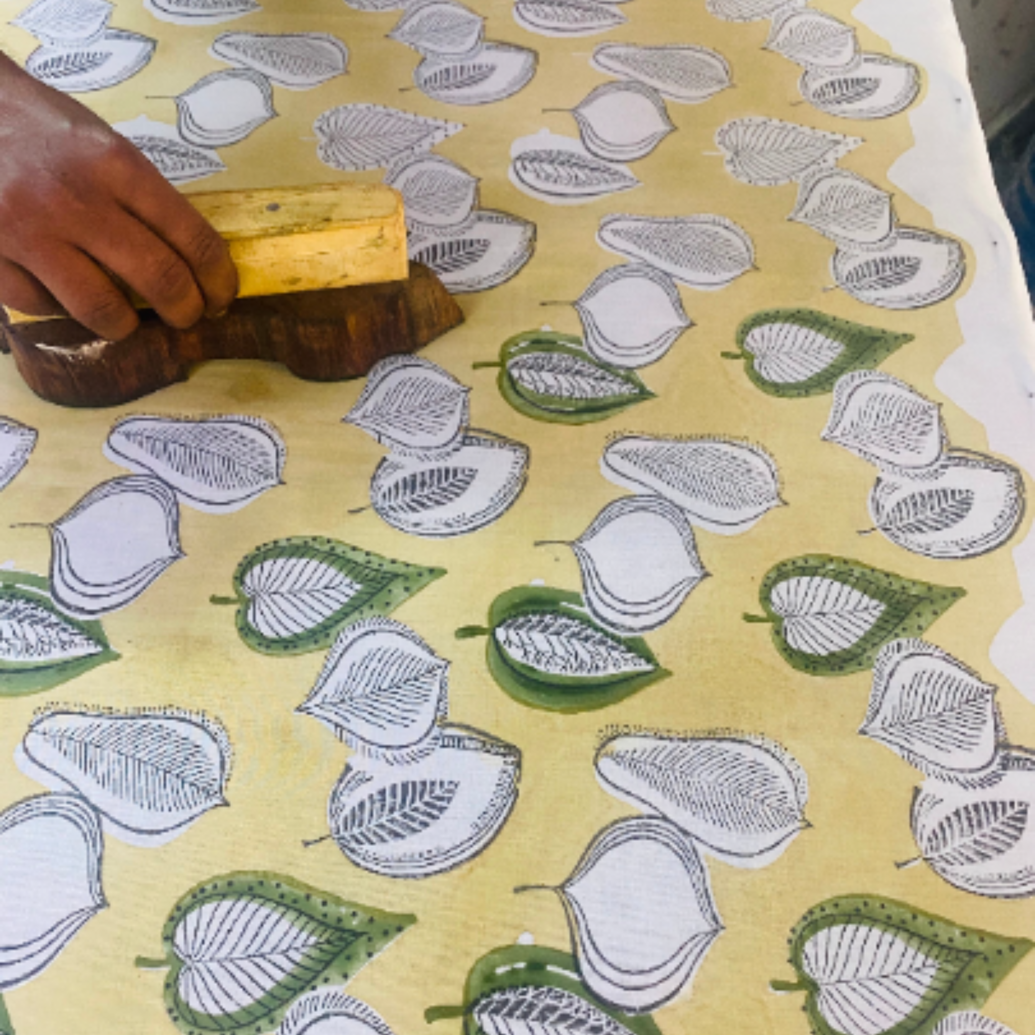 Hand applying a leaf pattern to fabric using a wooden block.