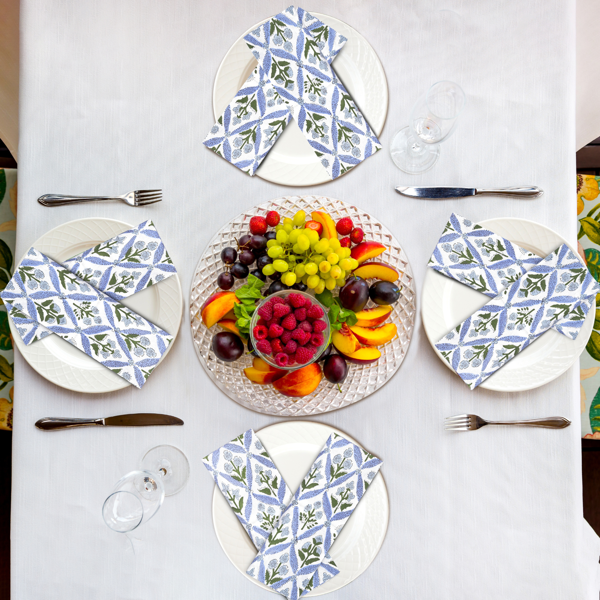 Table setting with plates, napkins, and a fruit platter on a white tablecloth.