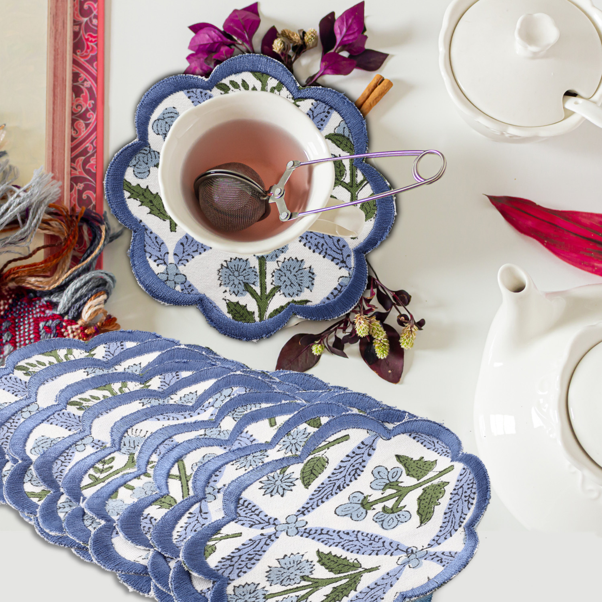 Set of blue floral coasters with a cup of tea and teapot on a white surface.