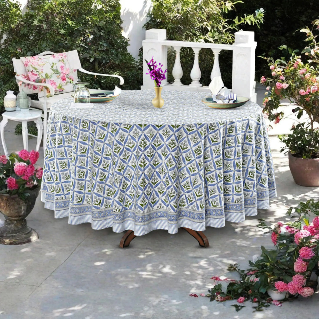 Outdoor table setting with a patterned tablecloth, chairs, and floral arrangements.