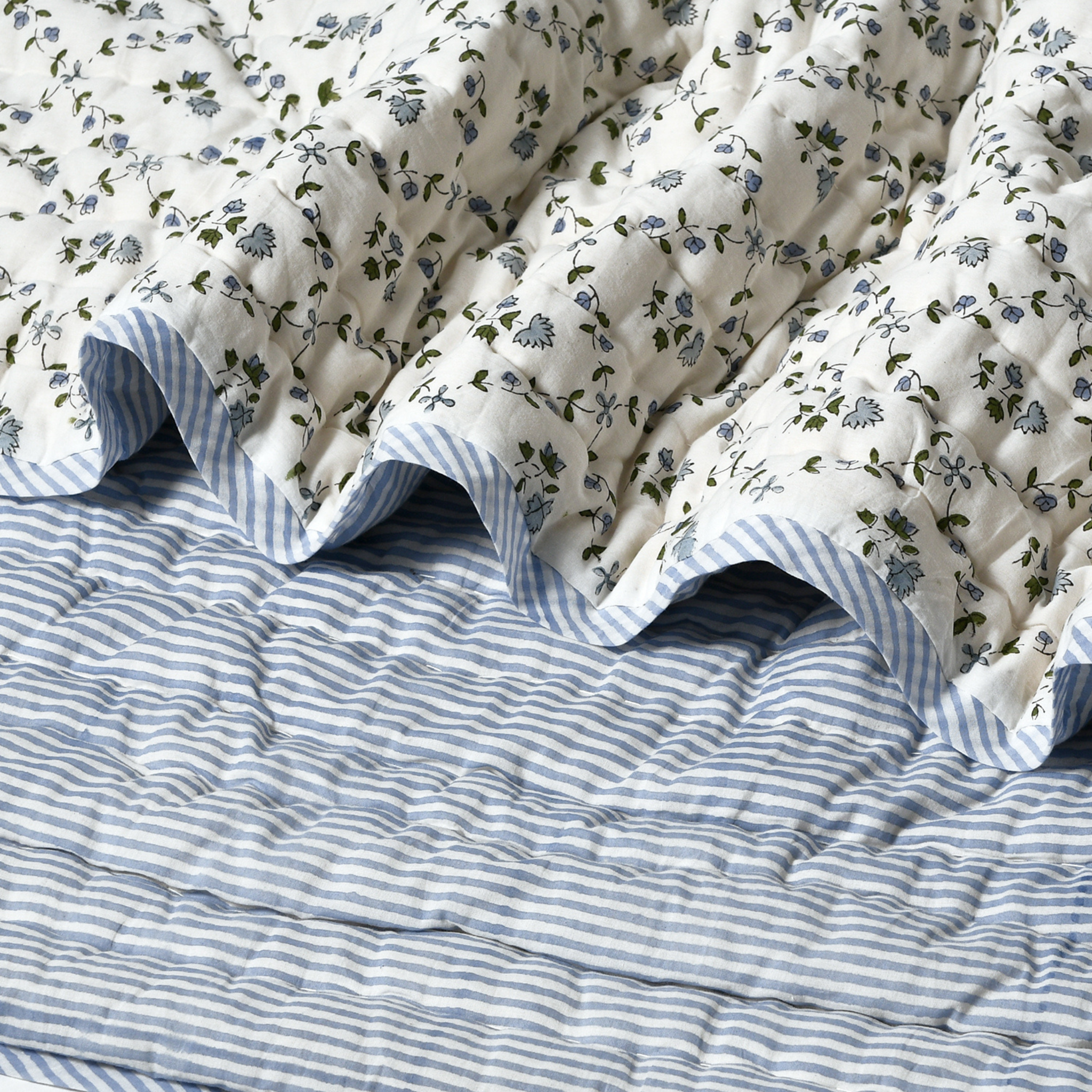Floral-patterned quilt on a bed with blue and white striped bedding