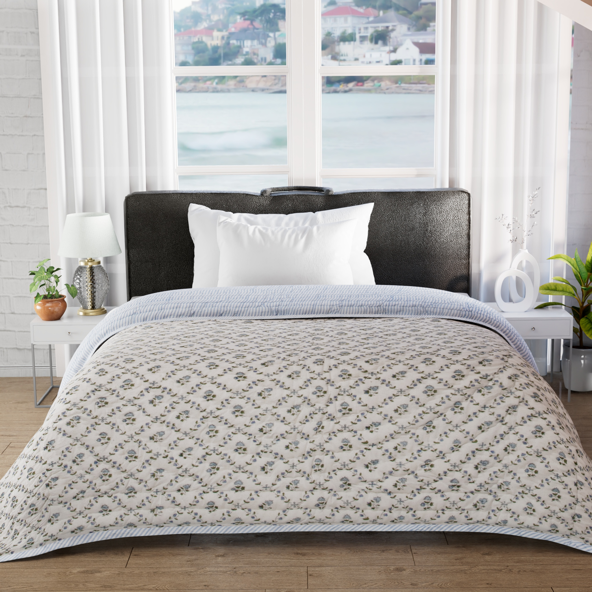 Bed with floral-patterned comforter in a room with large windows and plants.