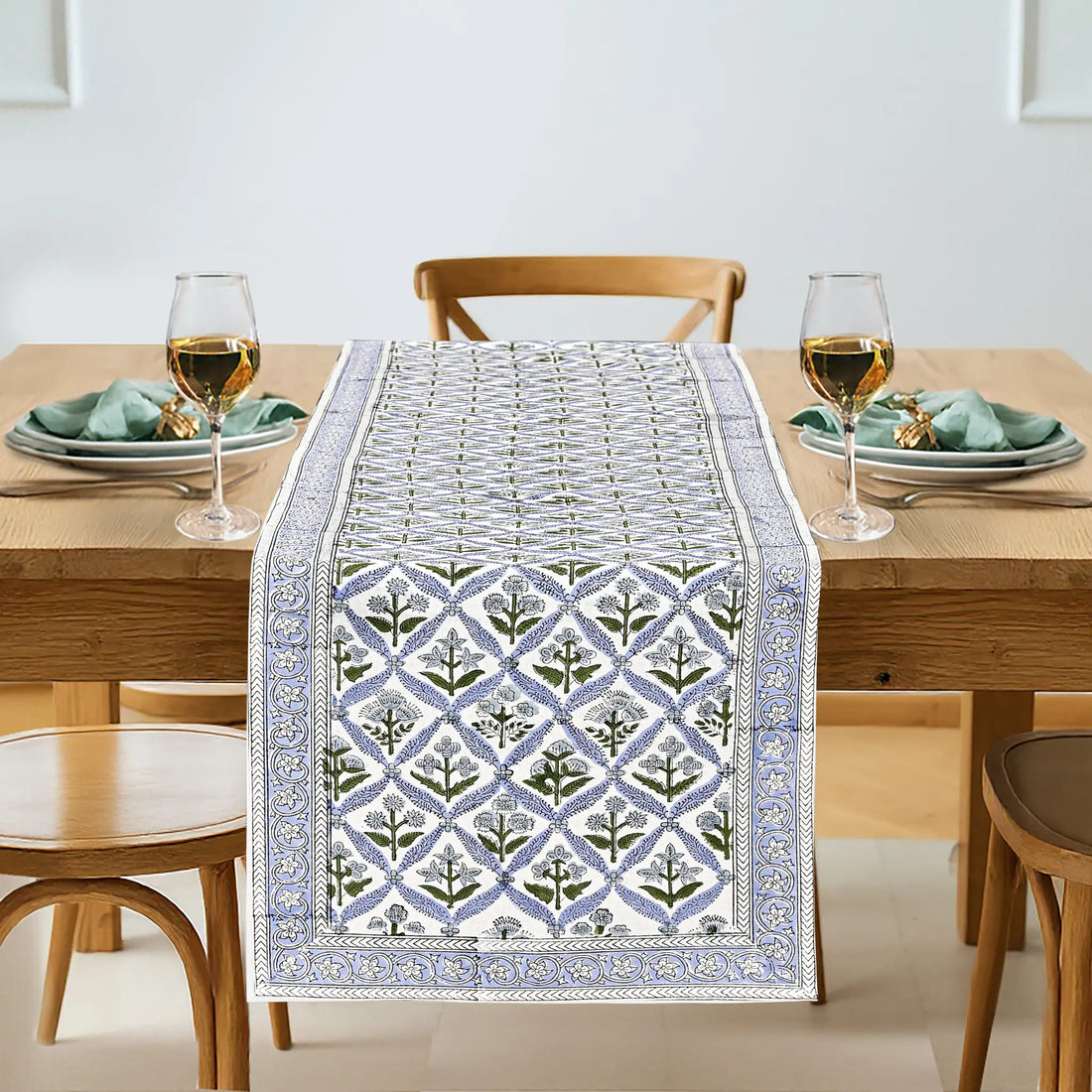 Dining table set with a patterned table runner, glasses, and plates.