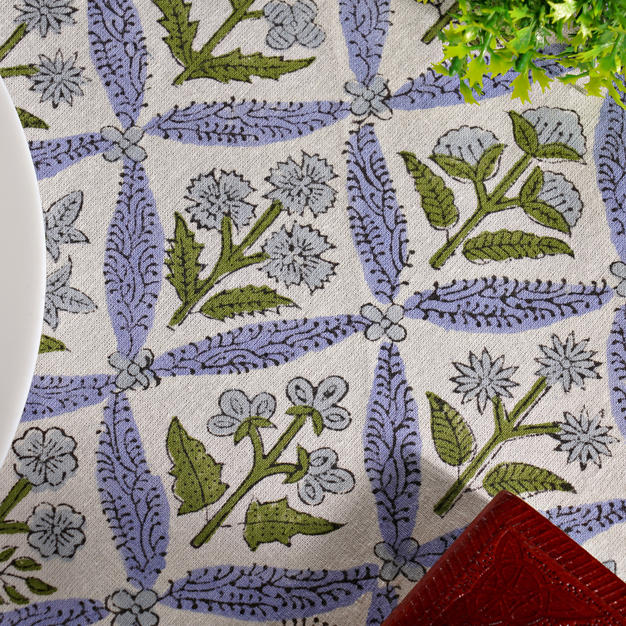 Close-up of a floral patterned fabric with green leaves and purple flowers on a white background.