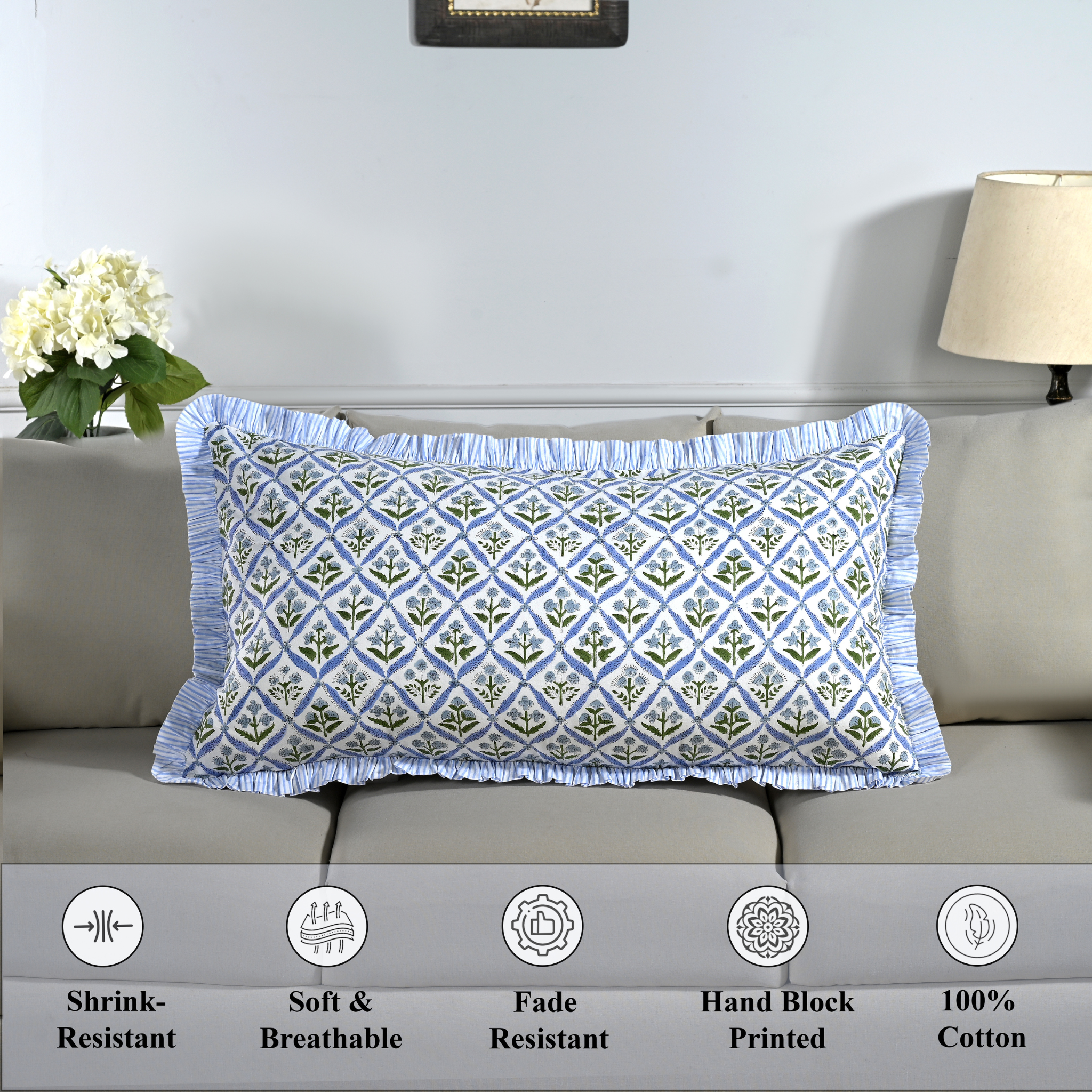 Cotton block print pillow cover placed on a bed with lamp and flowers in background.