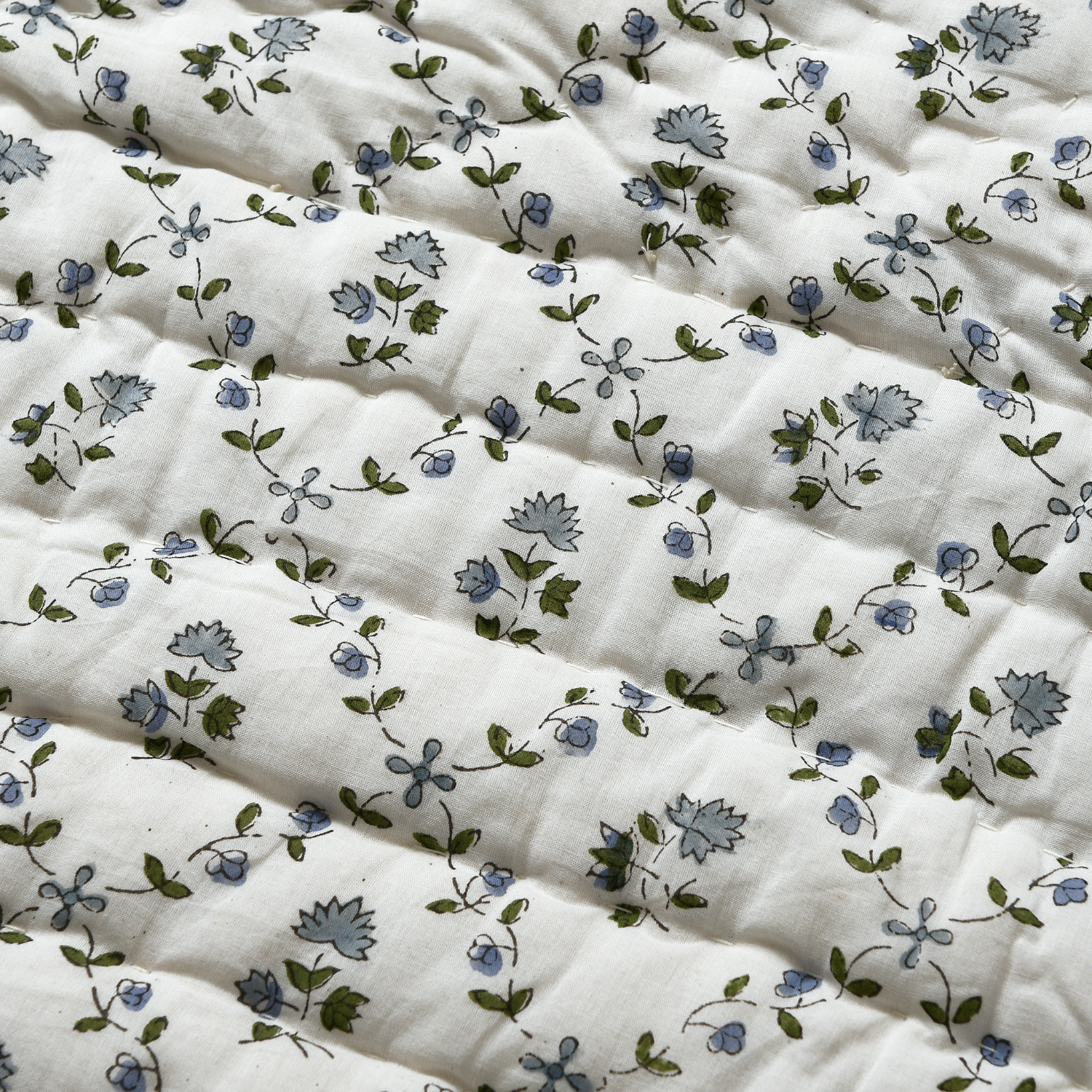 Floral patterned fabric with blue flowers and green leaves on a white background