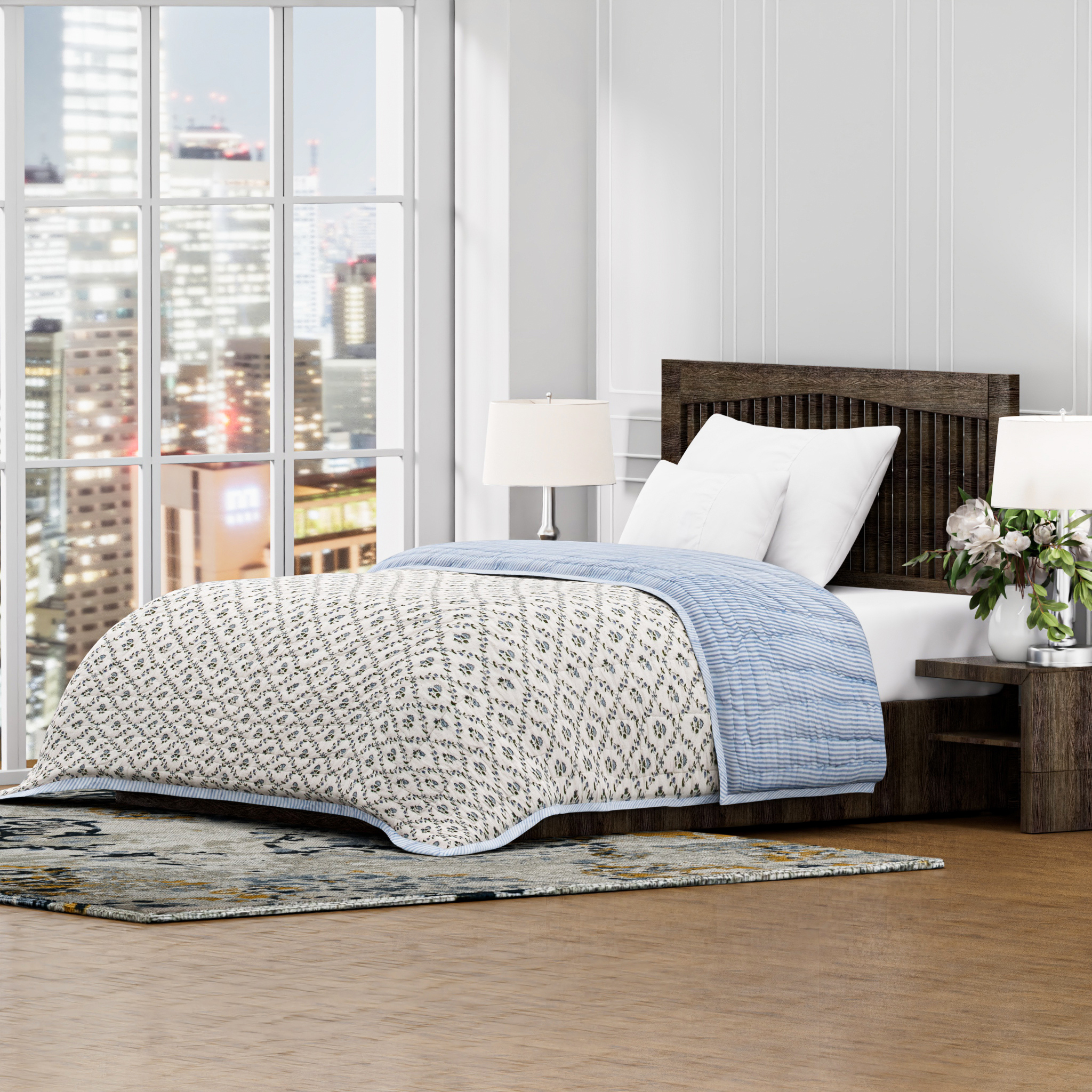 Bedroom with a bed featuring a patterned quilt and city view from large windows.