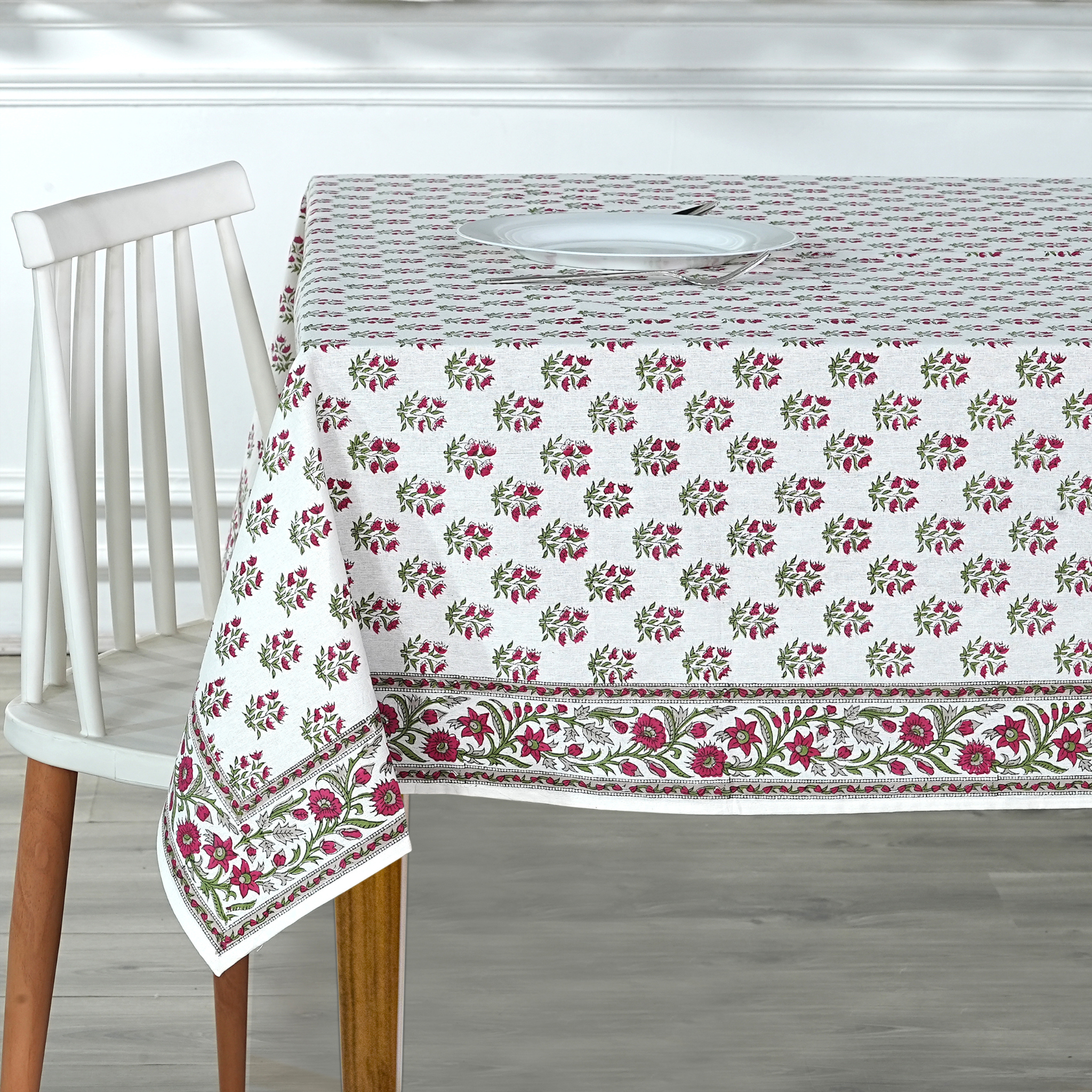 Floral patterned tablecloth on a wooden table with a chair.