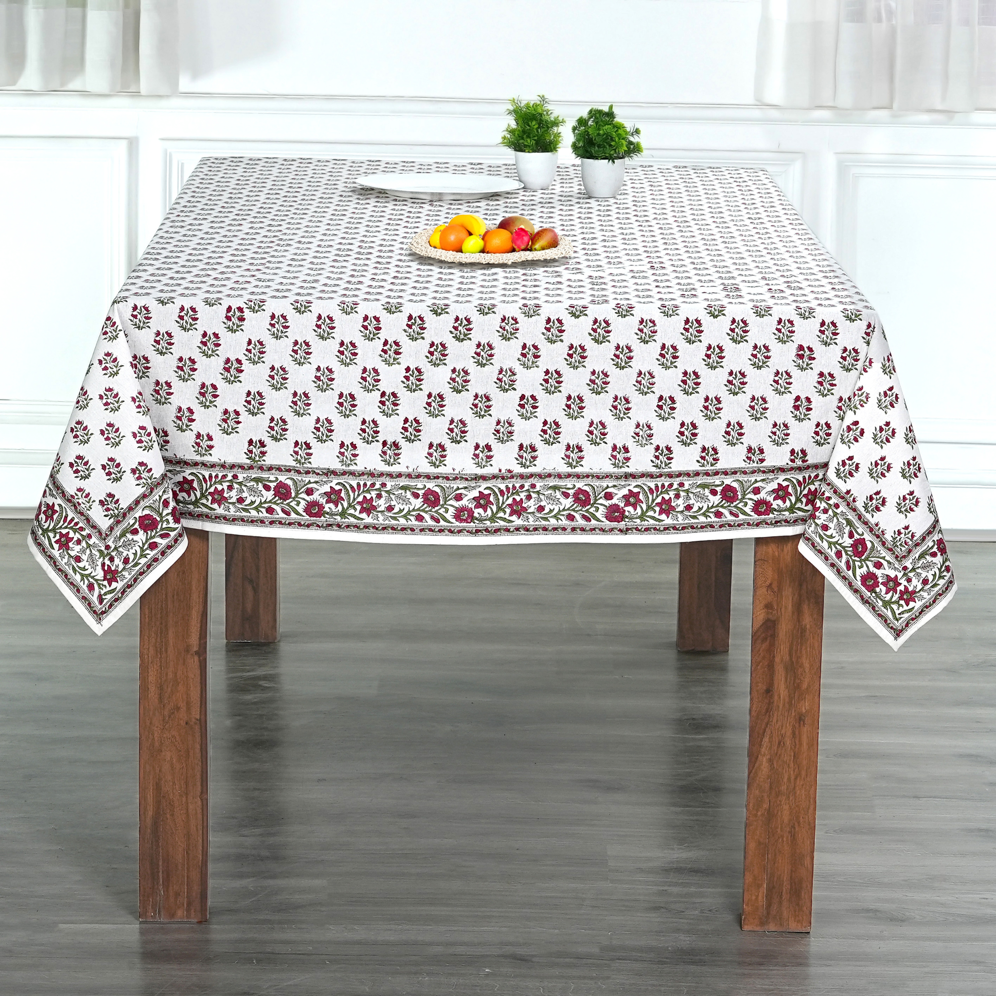 Tablecloth with floral pattern on a wooden table in a room with white walls.