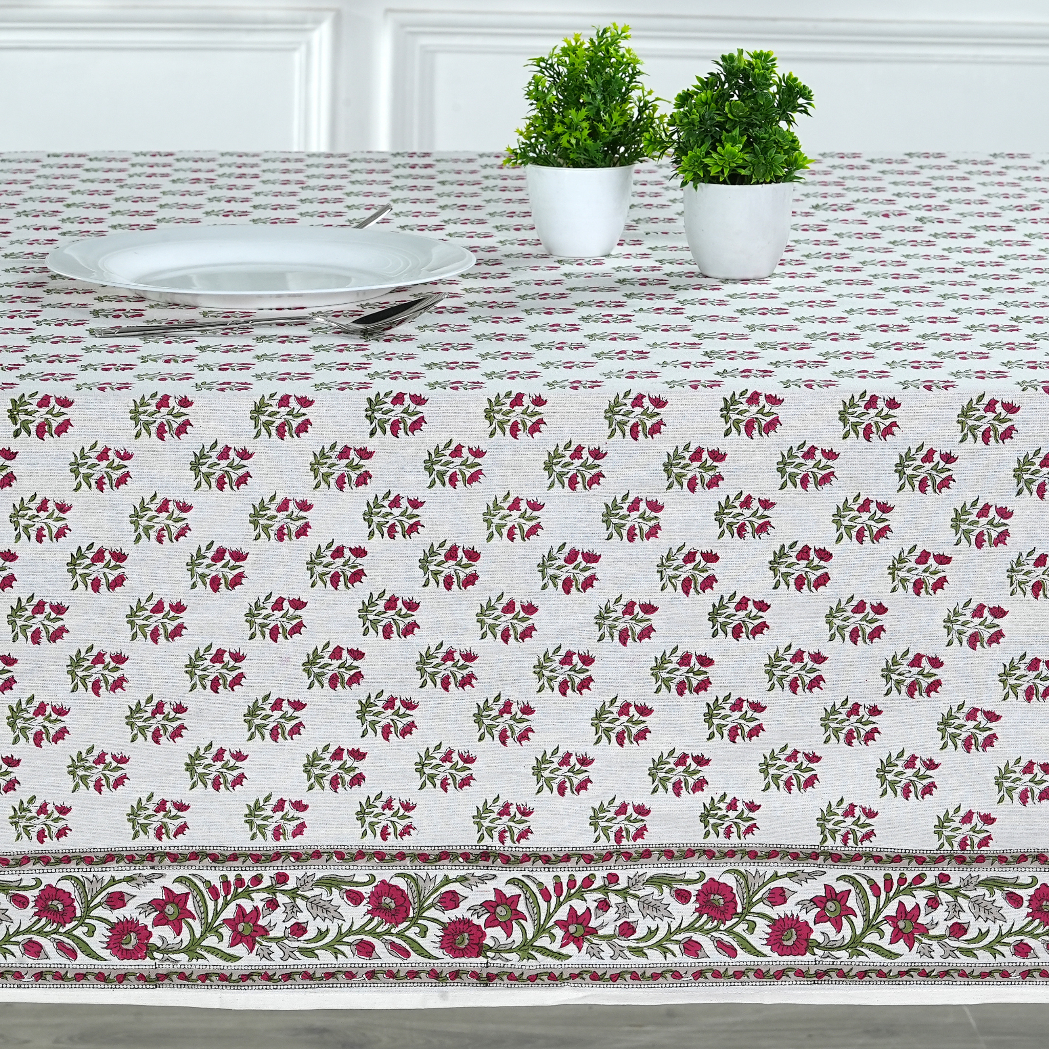 Floral patterned tablecloth on a table with two potted plants and a white plate.