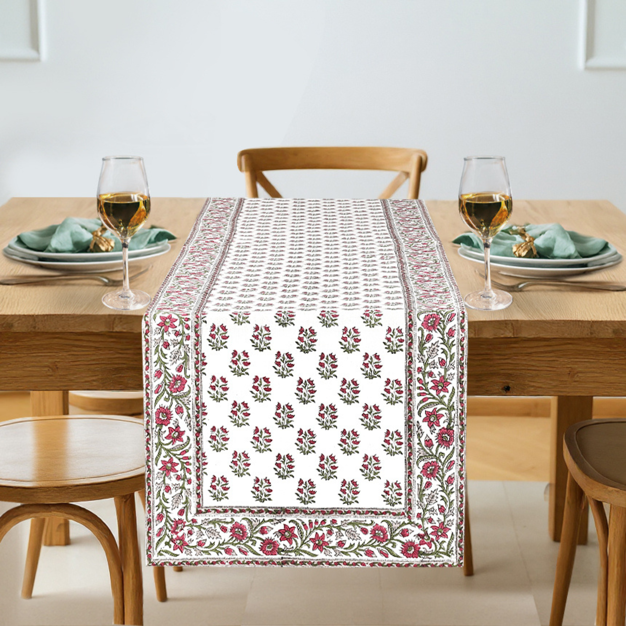 Dining table with a floral patterned table runner, glasses, and plates.