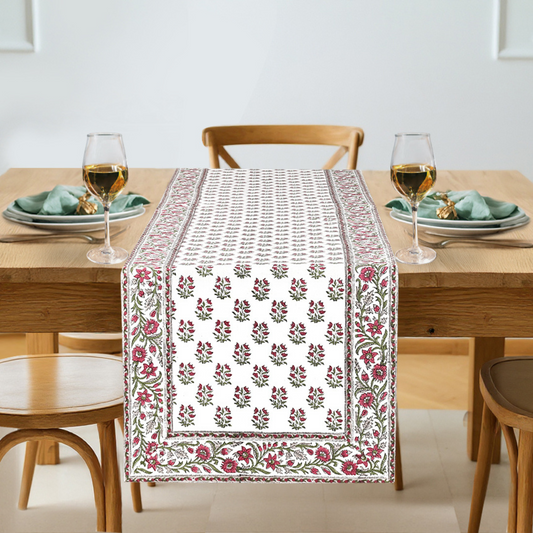 Dining table with a floral patterned table runner, glasses, and plates.