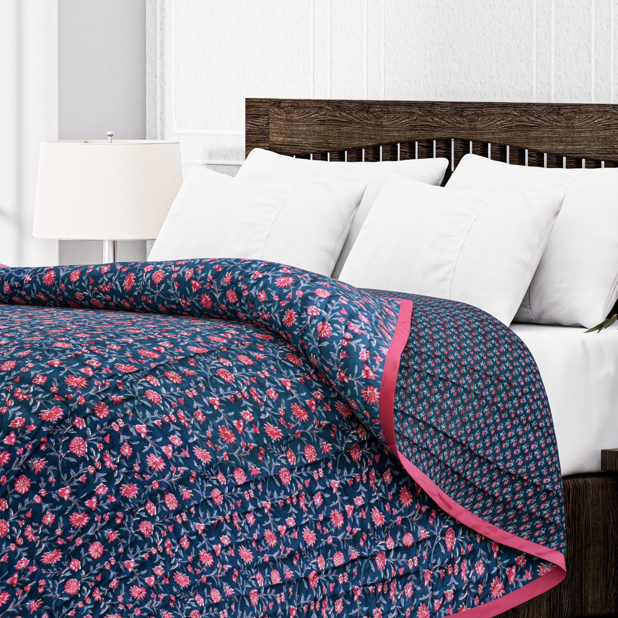 Navy blue floral quilt with pink trim on a bed with white pillows and wooden headboard.