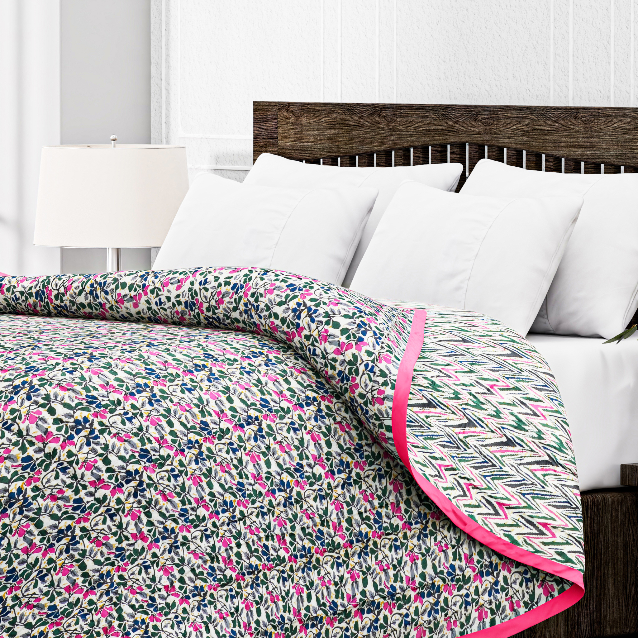 Floral patterned quilt with pink border on a bed with white pillows and wooden headboard.