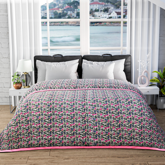 Bed with floral patterned comforter in a room with large windows showing a waterfront view.