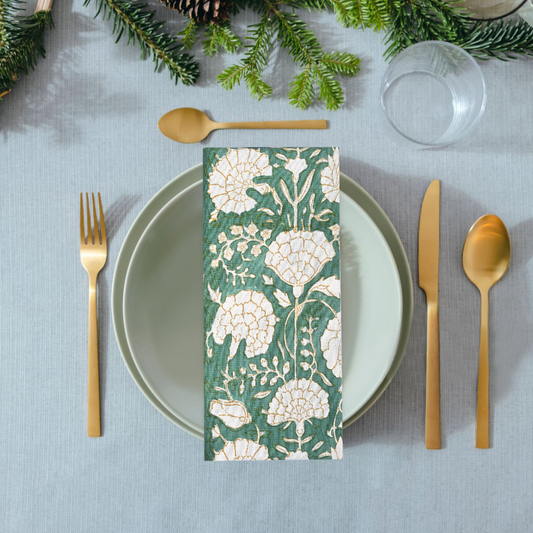 Table setting with a floral napkin, gold cutlery, and greenery on a gray tablecloth.