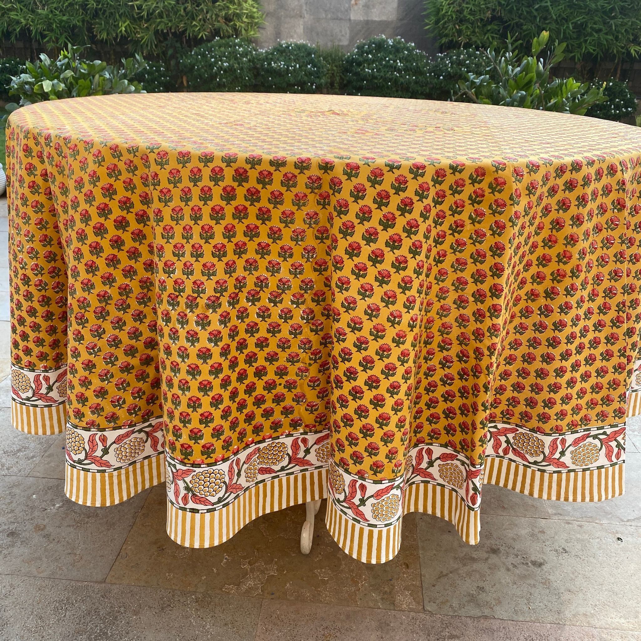 Round table covered with a yellow floral patterned tablecloth outdoors.