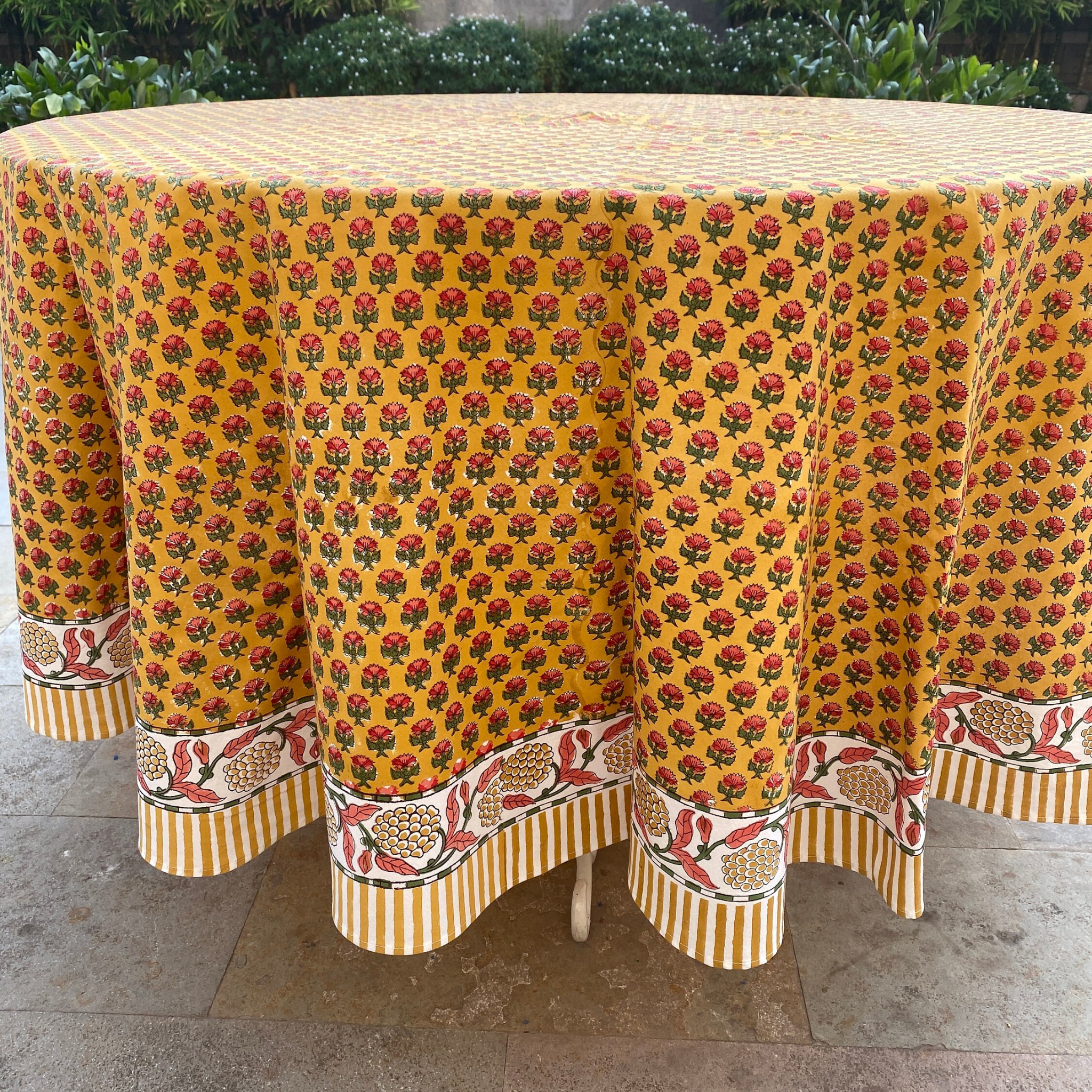 Round table with a yellow floral patterned tablecloth on a stone surface.