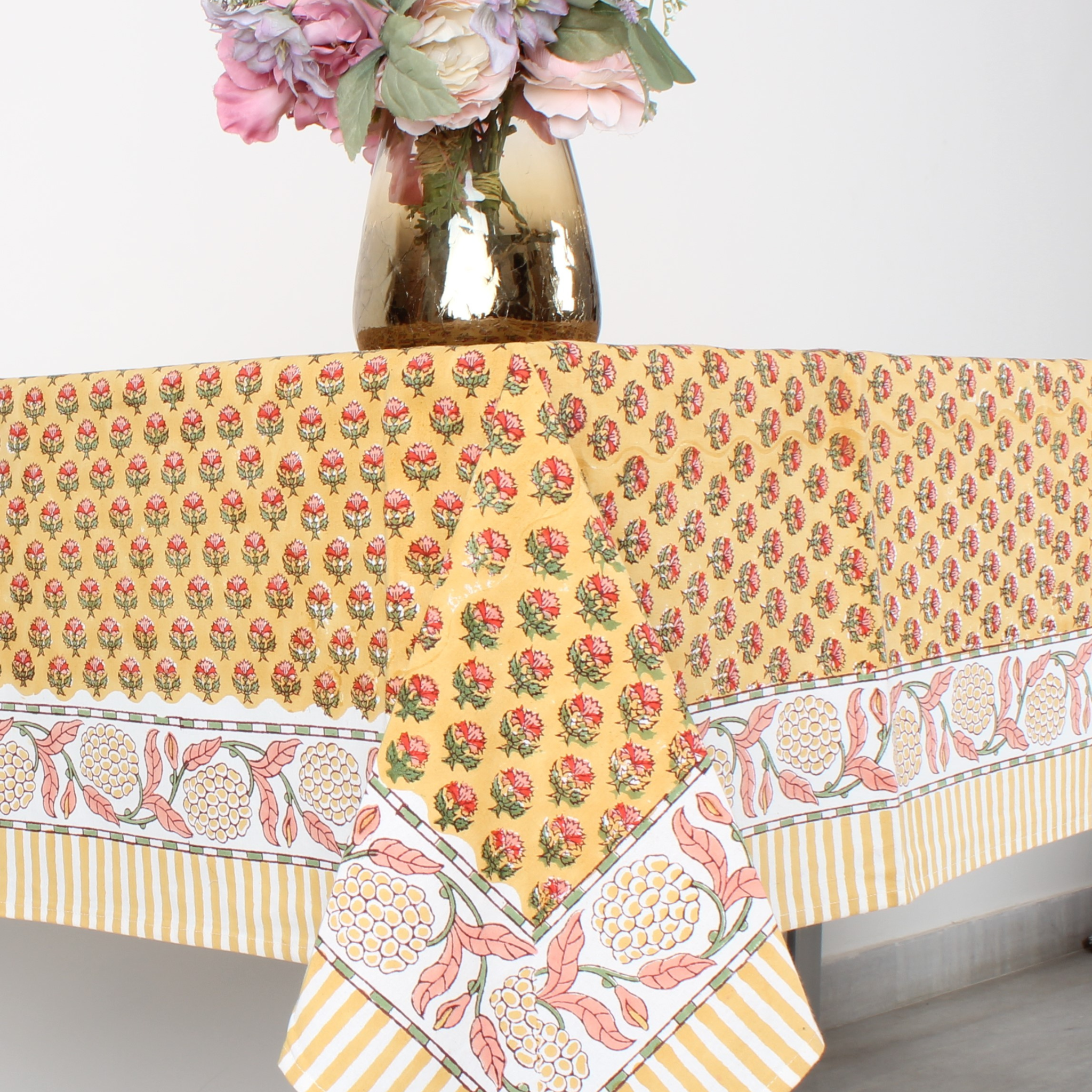 Yellow floral patterned tablecloth on a table with a vase of flowers.