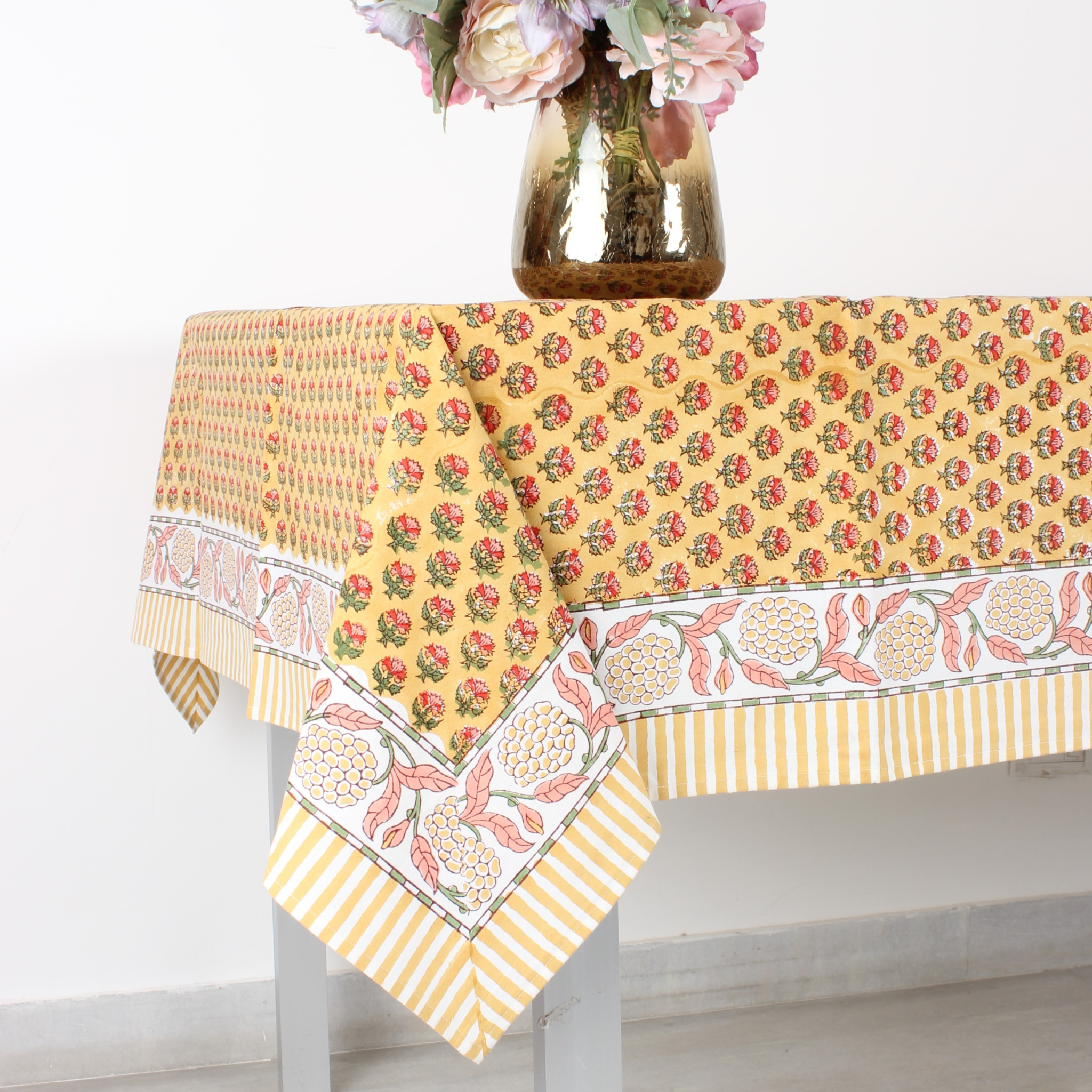 Yellow floral patterned tablecloth on a white table with a vase of flowers.